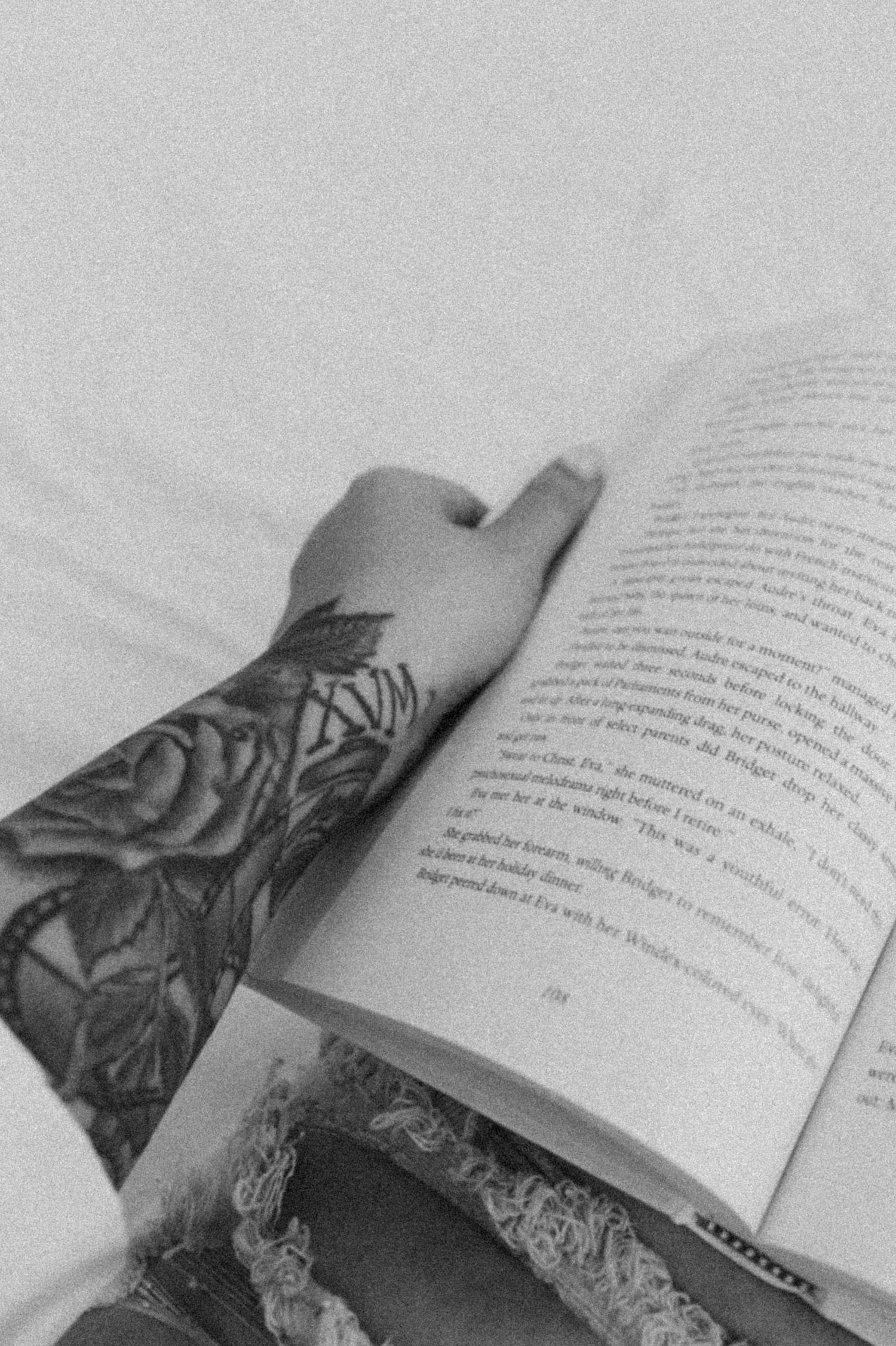 Open book with visible rose tattoo on arm in black and white photography.
