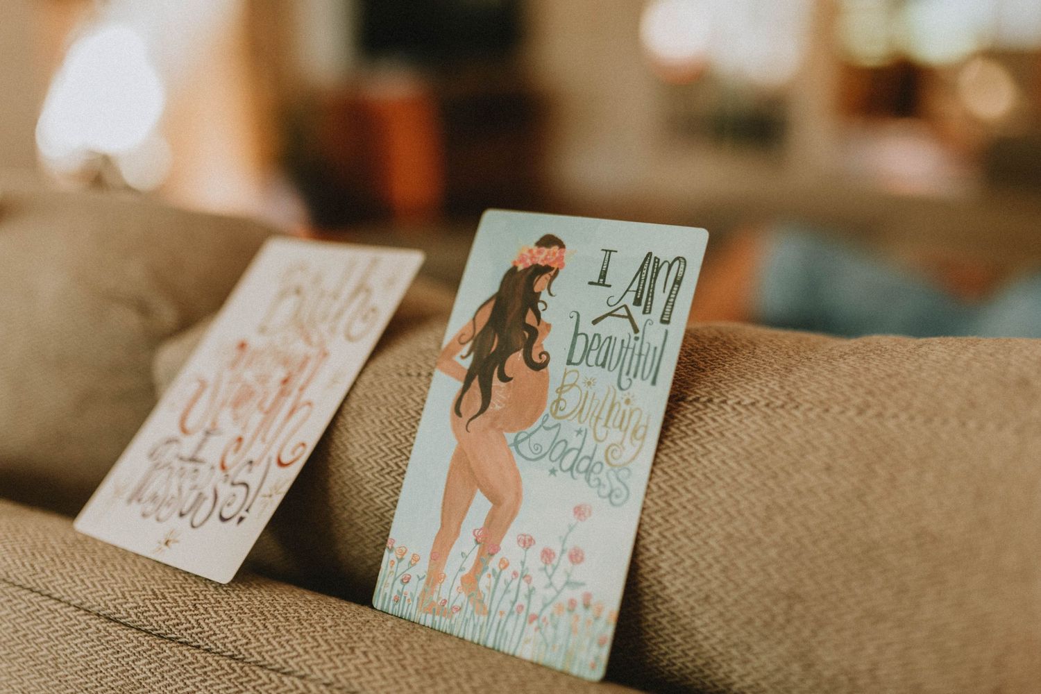 Two decorative greeting cards featuring whimsical illustrated designs rest on a textured burlap surface in soft lighting.