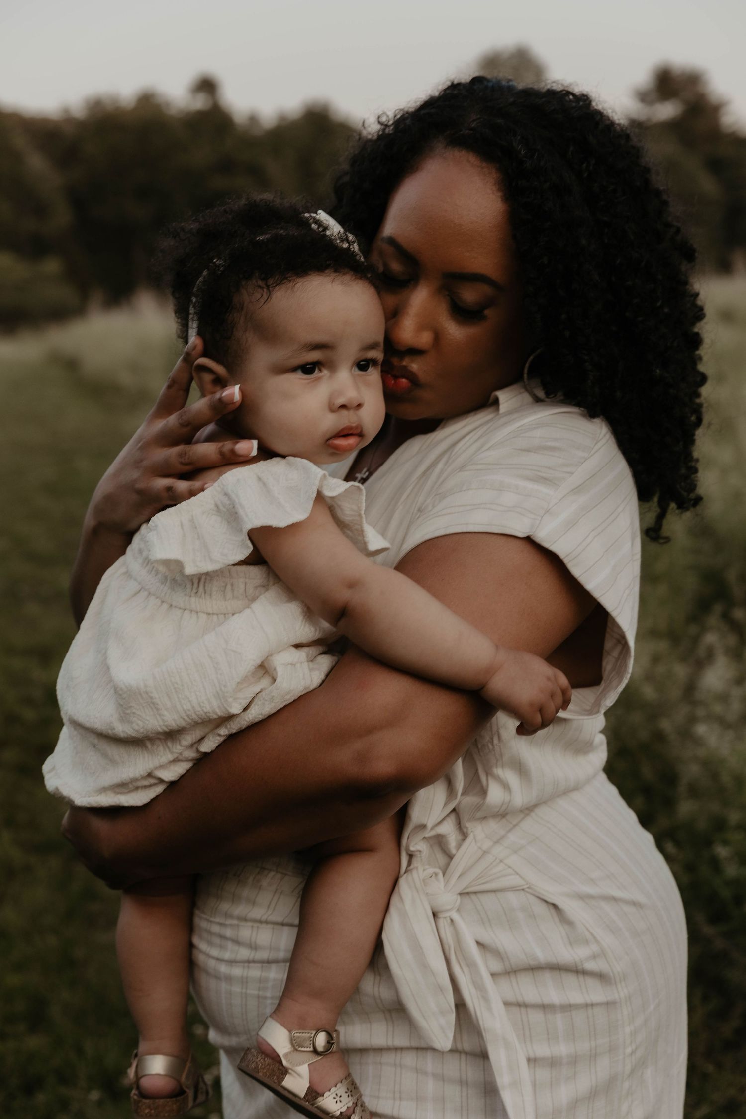 Tender moment captured between parent and toddler embracing outdoors during a moody photoshoot.
