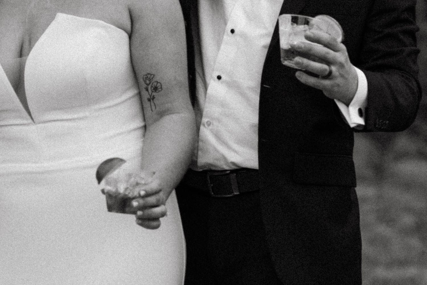 Black and white wedding photo showing close up of a couple's torso with bride in white dress with tattoo and groom in suit.