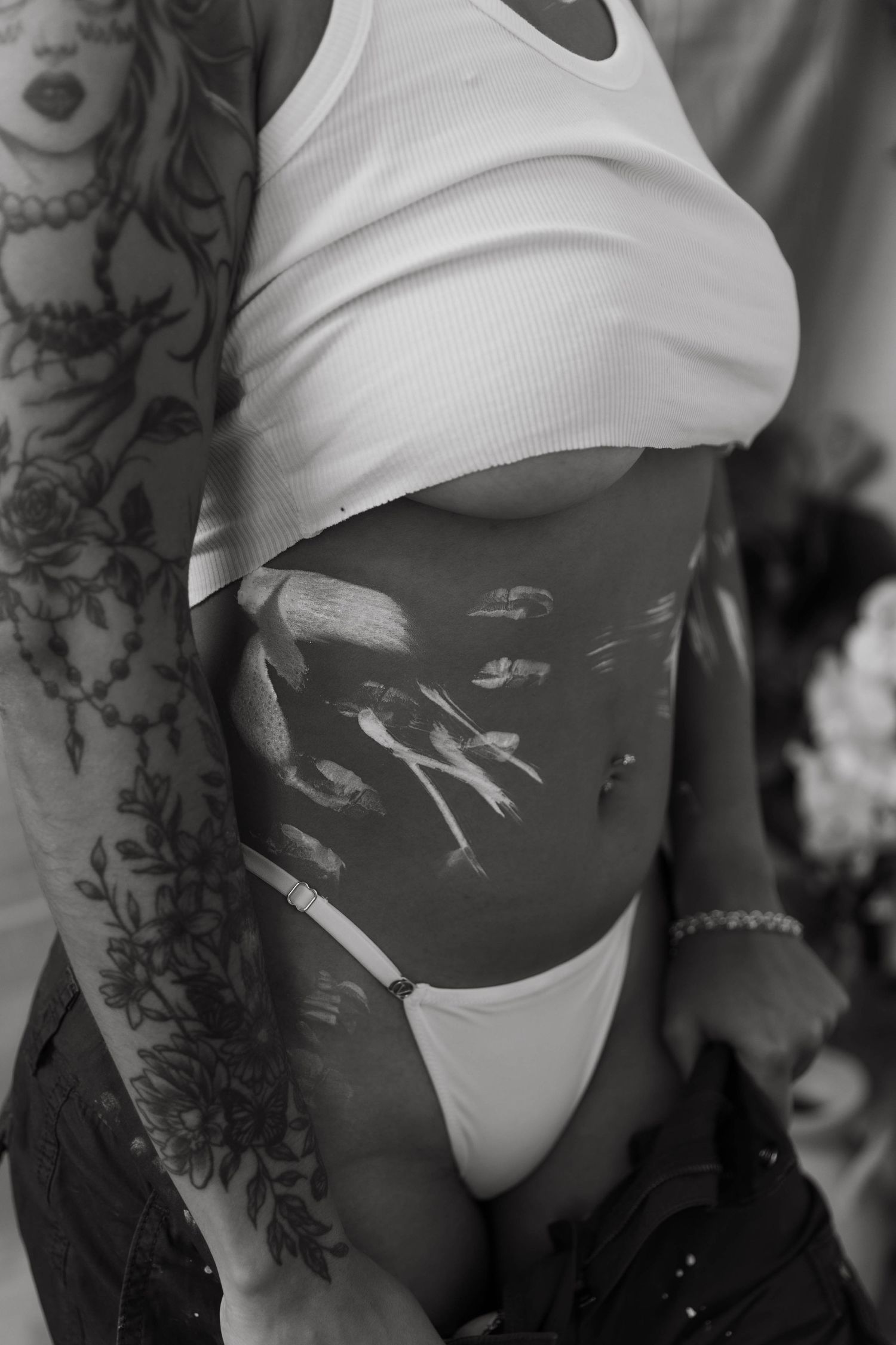 Artistic black and white photo showing torso with white tank top and tattoos.
