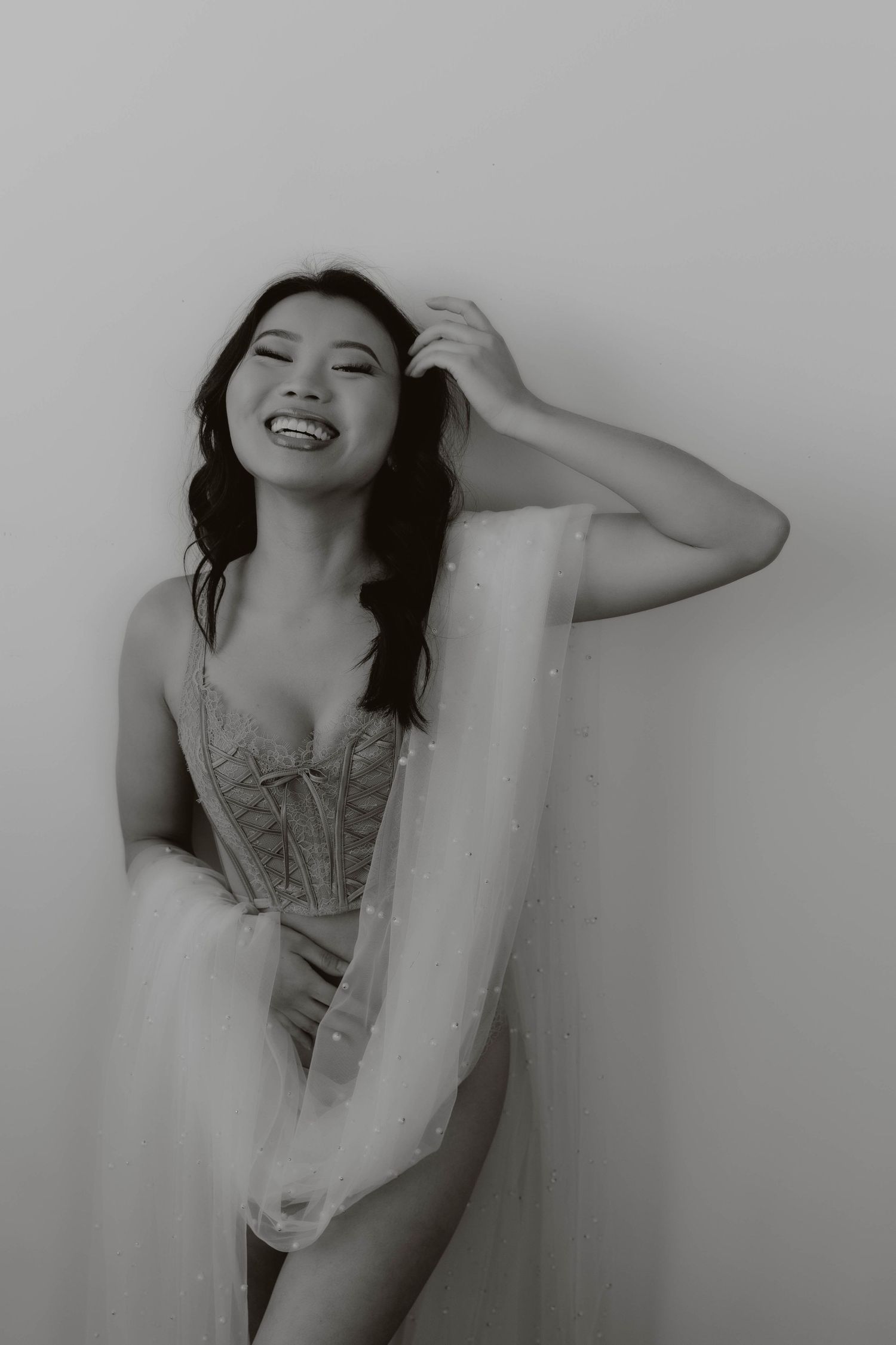 Black and white portrait of model in vintage-style corset with flowing sheer fabric overlay.