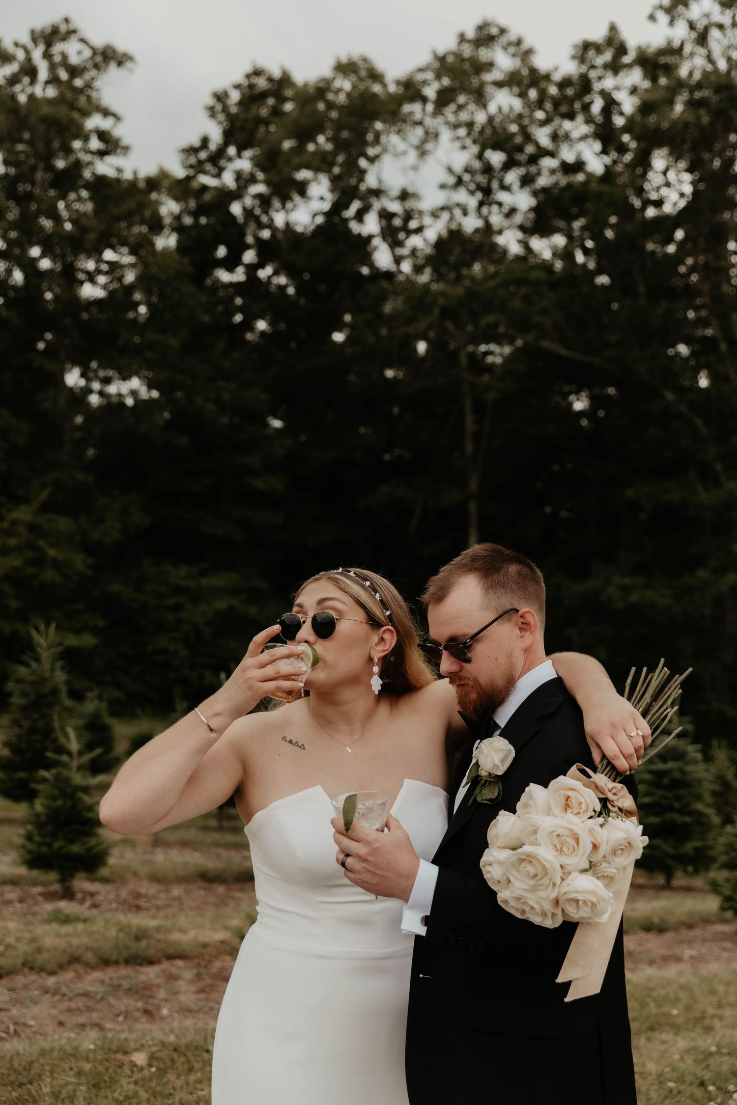 Newlywed couple shares playful candid moment at outdoor wedding with white roses.