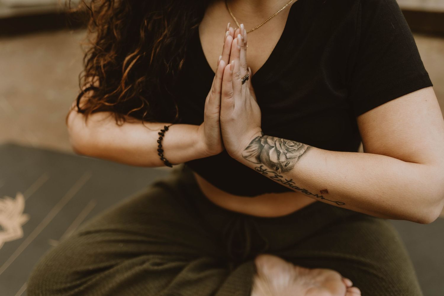 Person in black shirt practicing yoga meditation with prayer hands and visible arm tattoo.