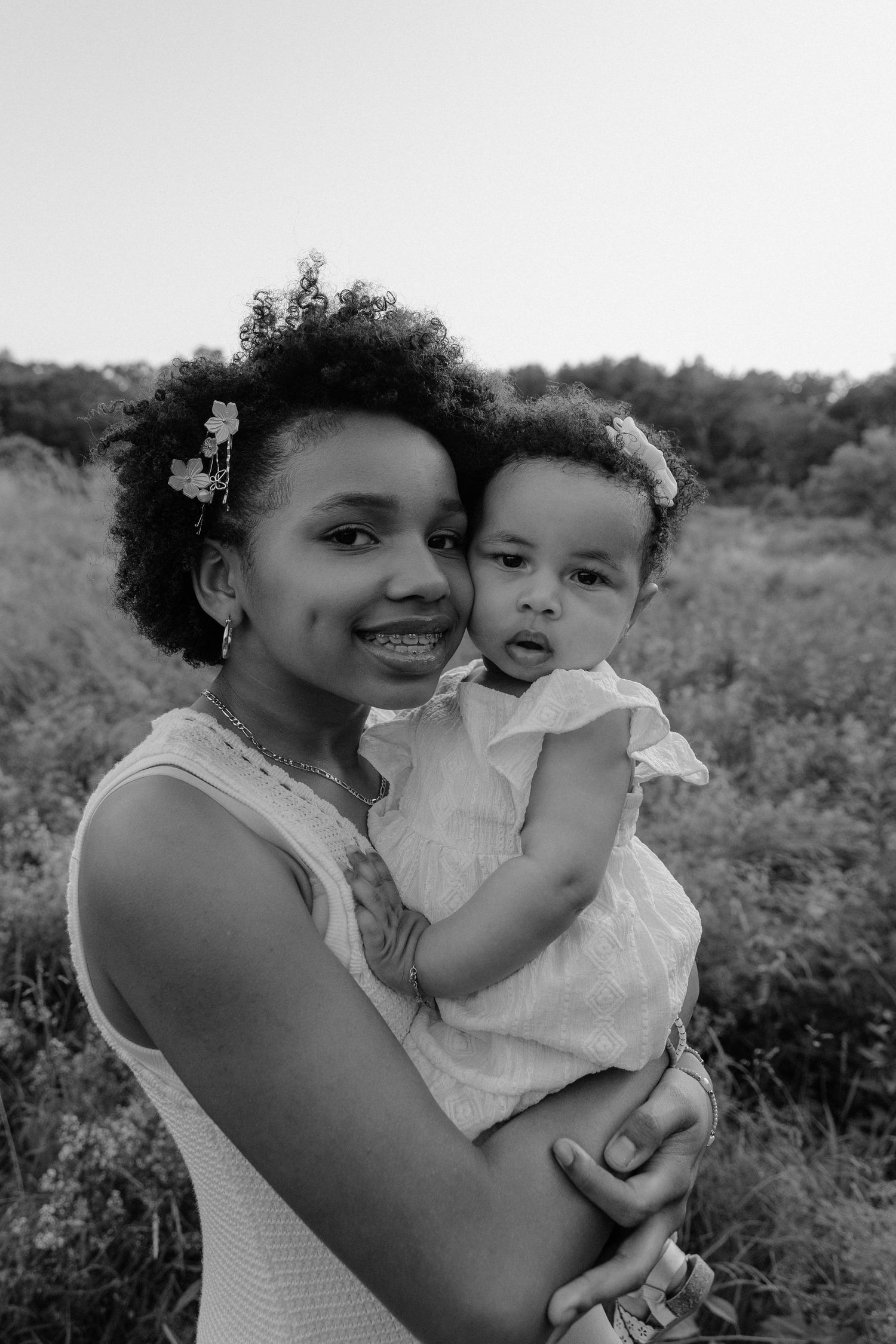 Black and white photos show tender moments between sisters outdoors in a natural setting.
