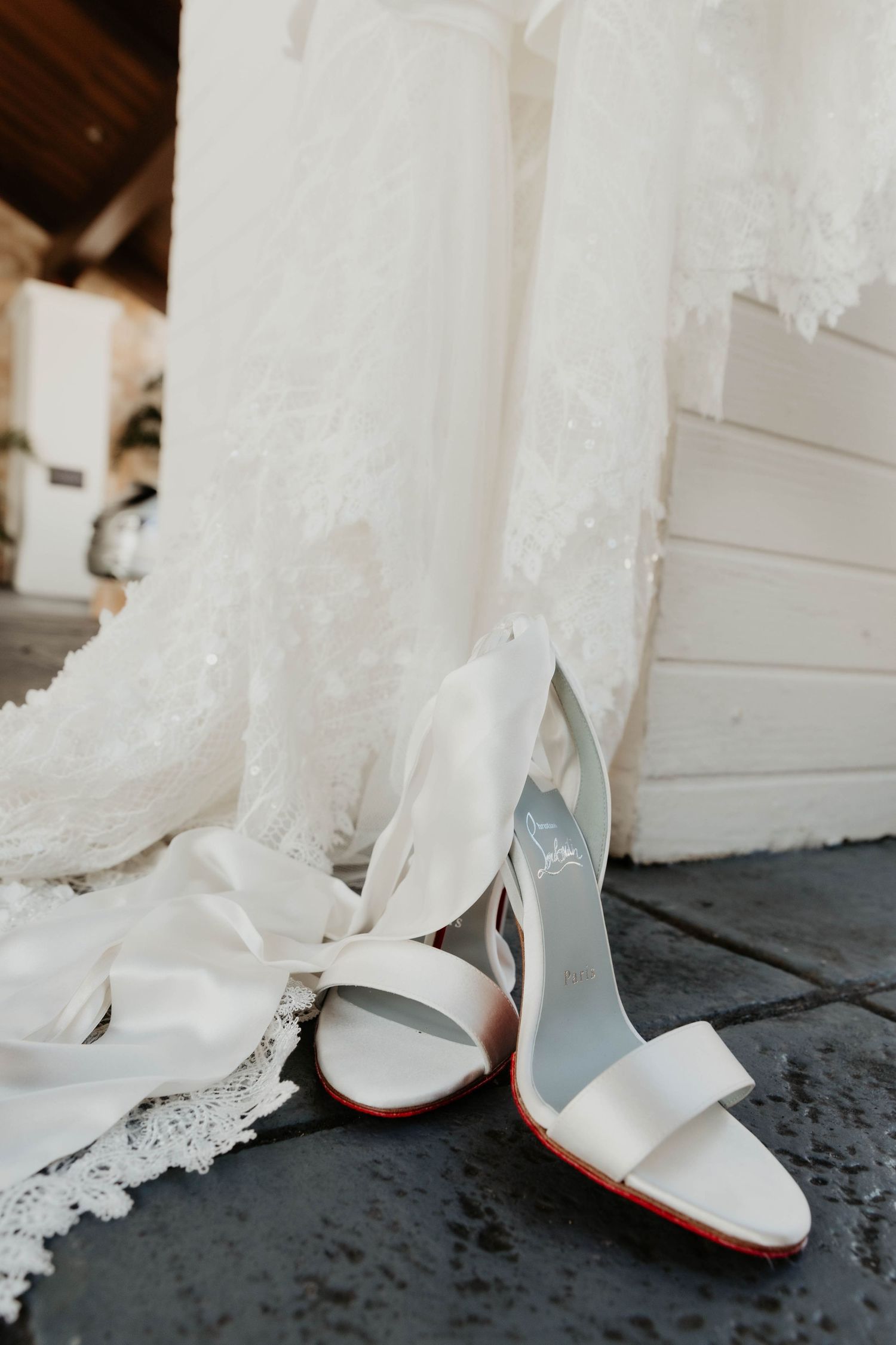 White bridal shoes displayed next to flowing lace wedding dress hem.