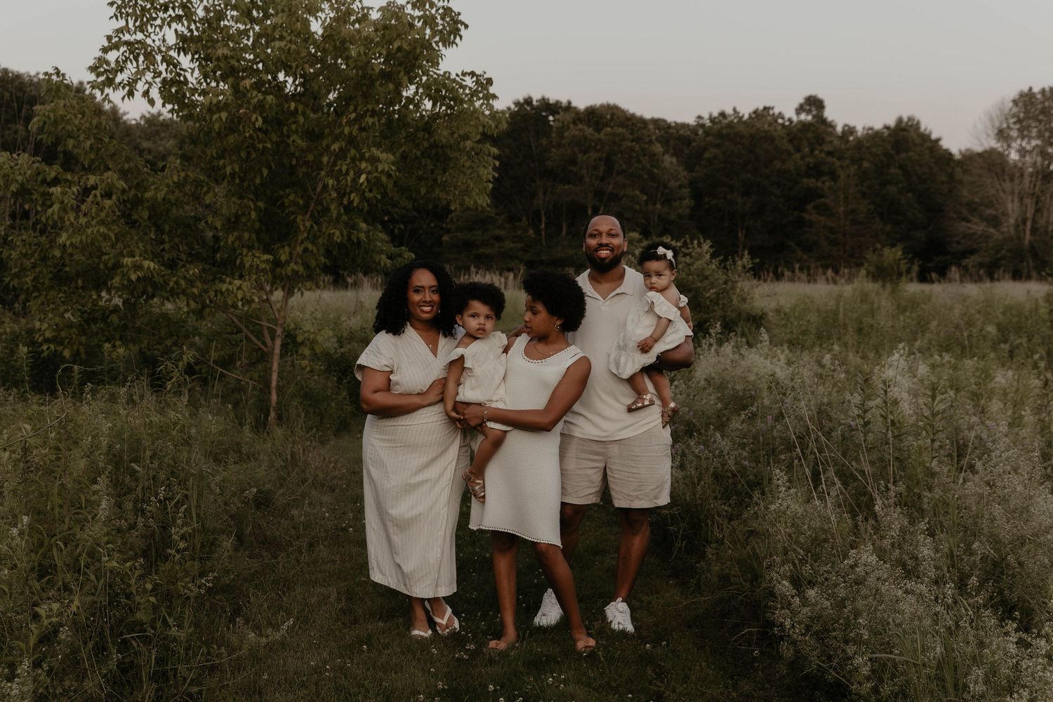 Group in white outfits poses together in a natural outdoor setting at dusk for a family photoshoot.