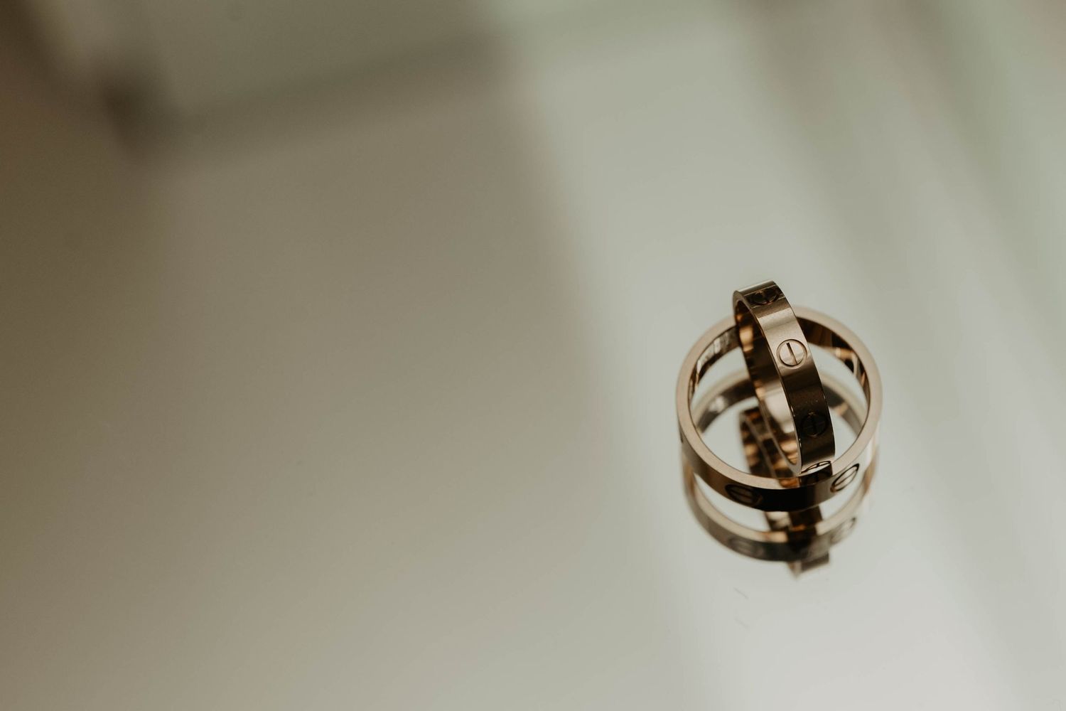 Two gold wedding rings shown close up with one suspended in air against a soft blurred background.