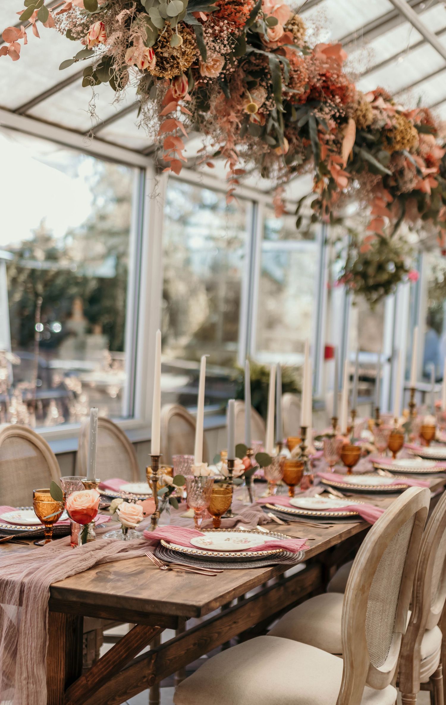 Elegant table setting with coral colored flowers hanging overhead in conservatory with glassware and place settings.