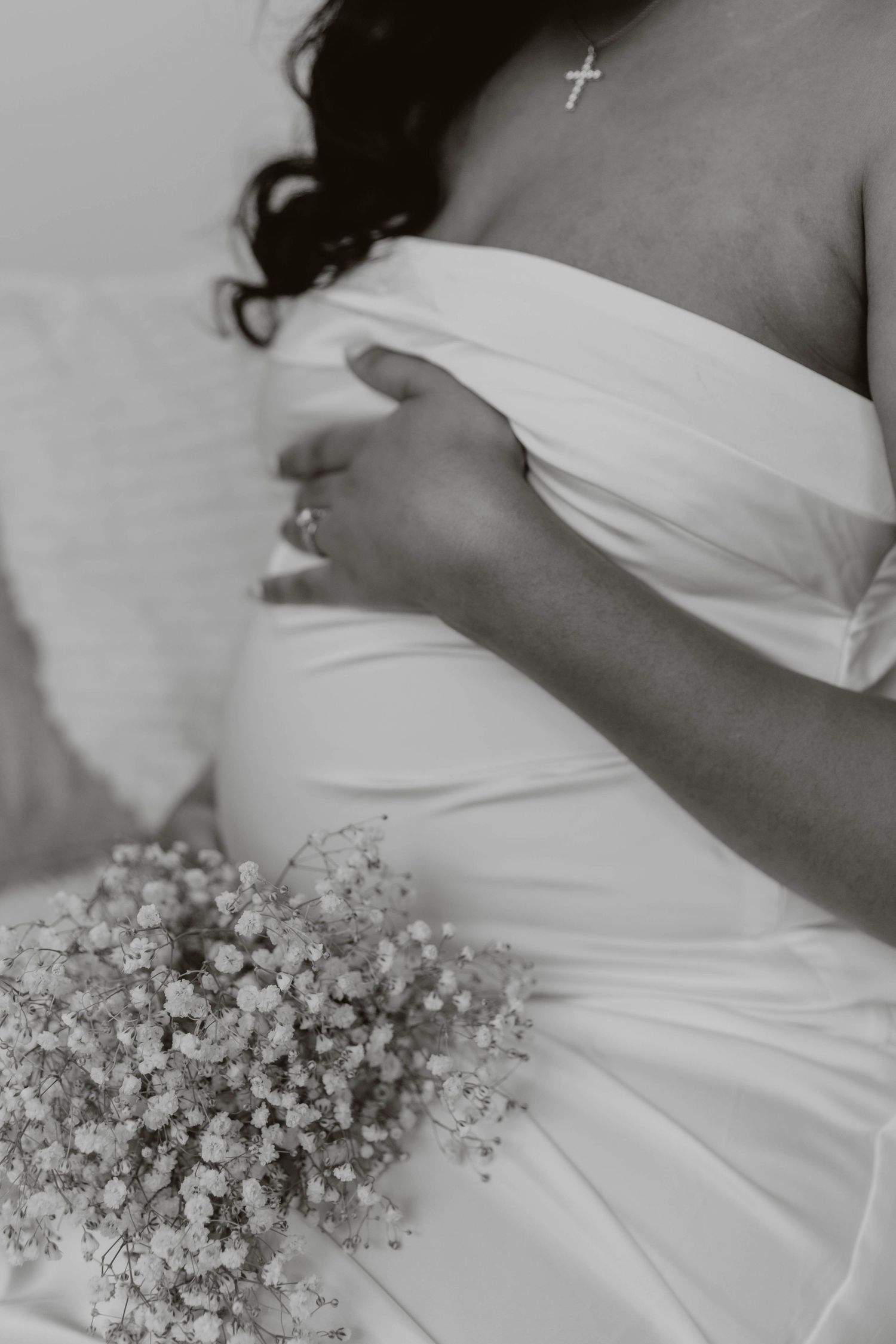 Black and white photo of a bridal dress with baby's breath bouquet and delicate cross necklace.