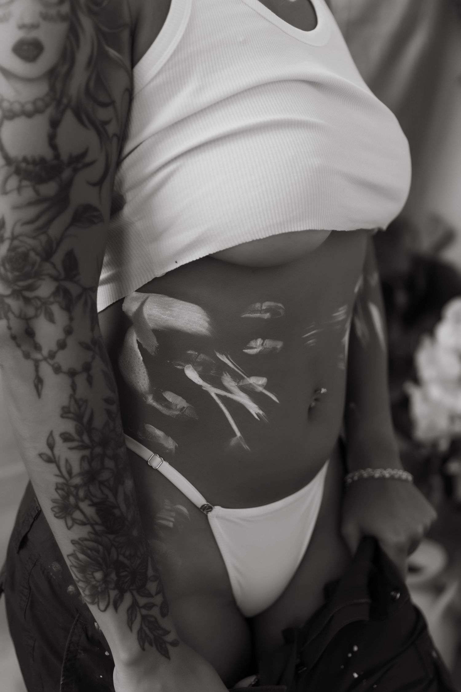 Black and white photograph showing torso with tattoos wearing white crop top and swimwear.