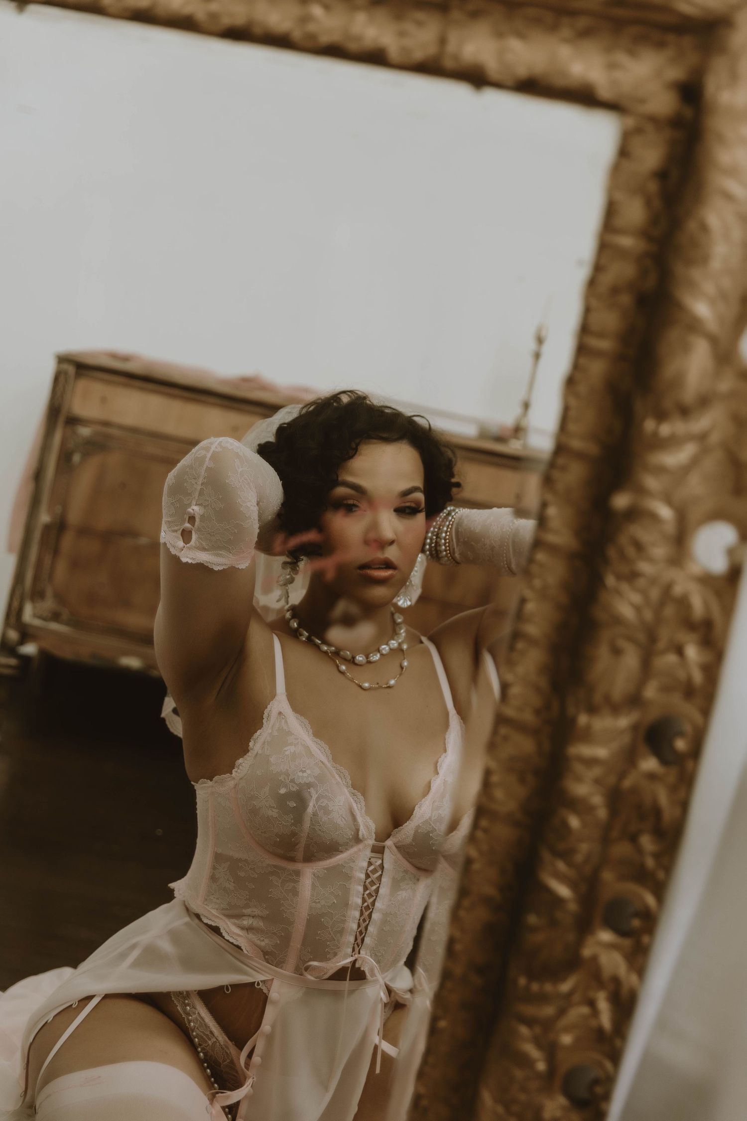 Vintage-inspired boudoir photograph in sepia tones featuring white lace lingerie and delicate jewelry.