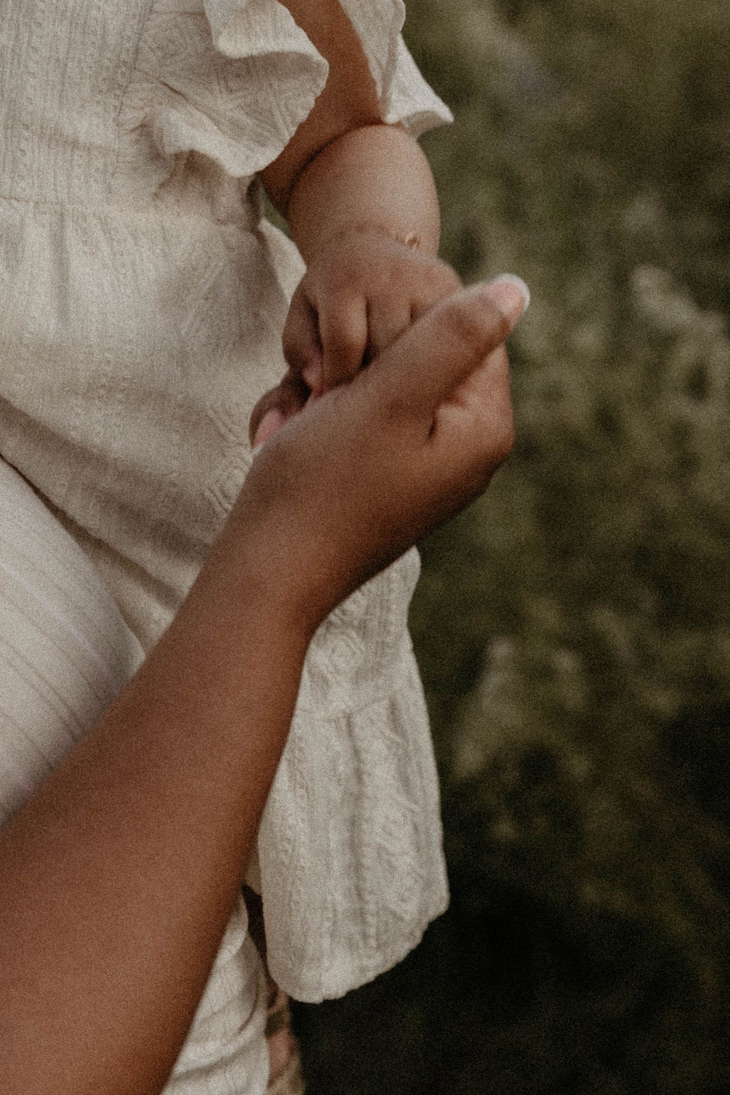A delicate close-up of hands gently holding white lace fabric against a dark background.