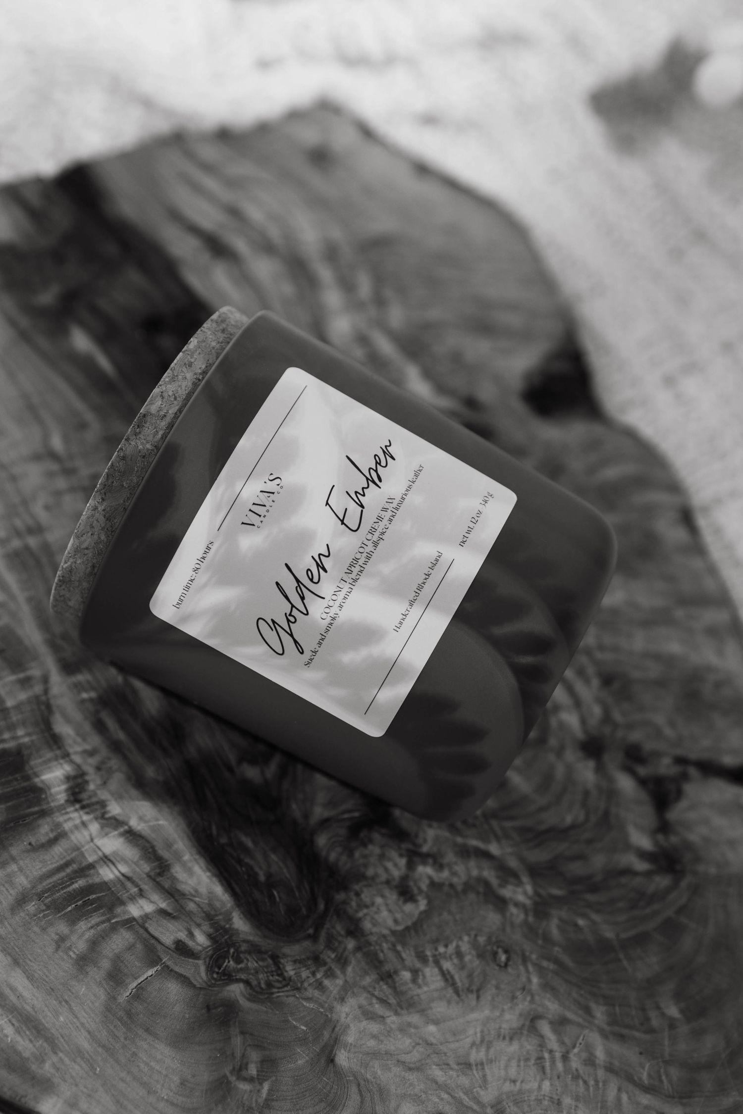 Black and white photo of a labeled glass candle jar on a textured wooden surface.