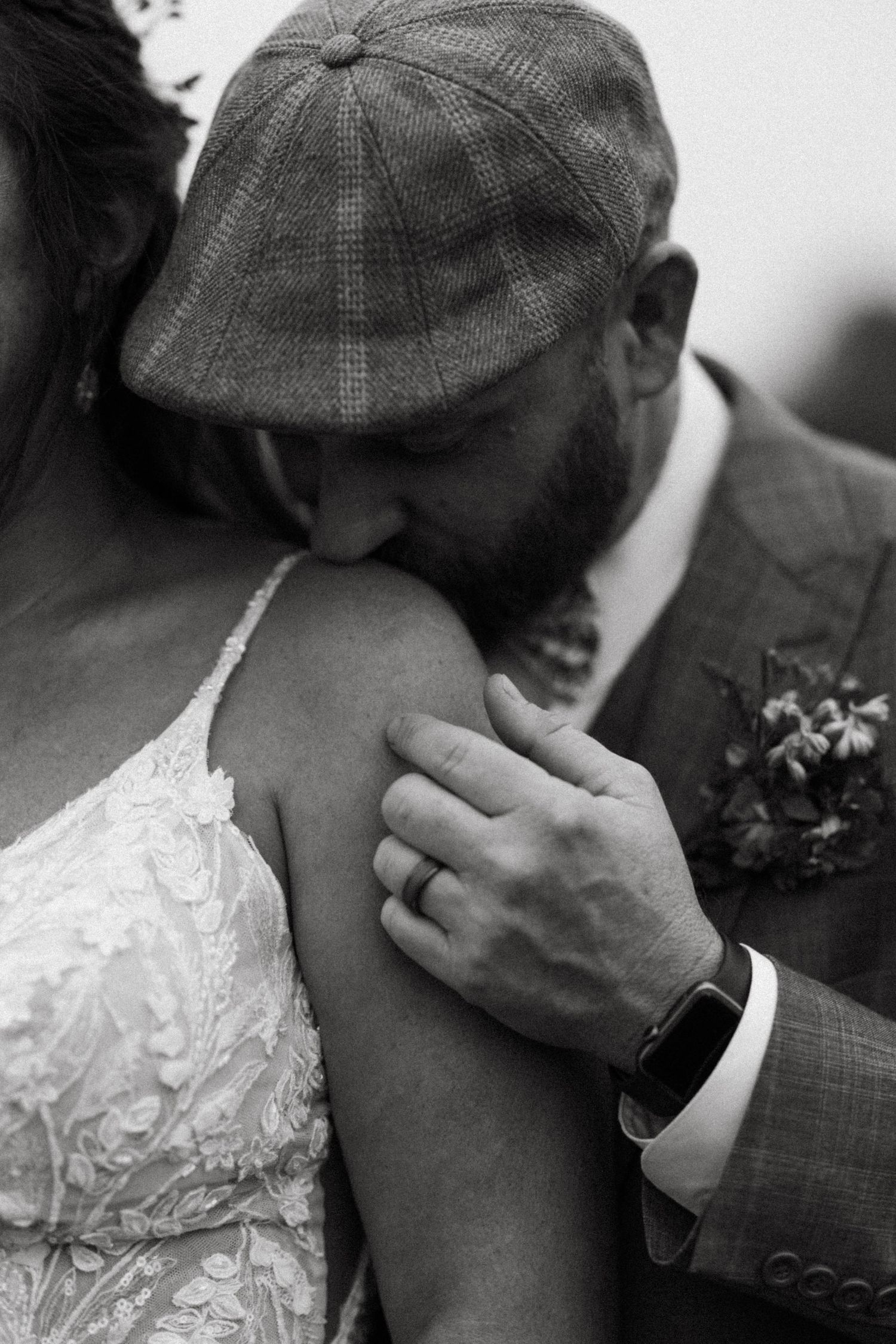Black and white image of an intimate moment between newlyweds, with groom wearing a flat cap.