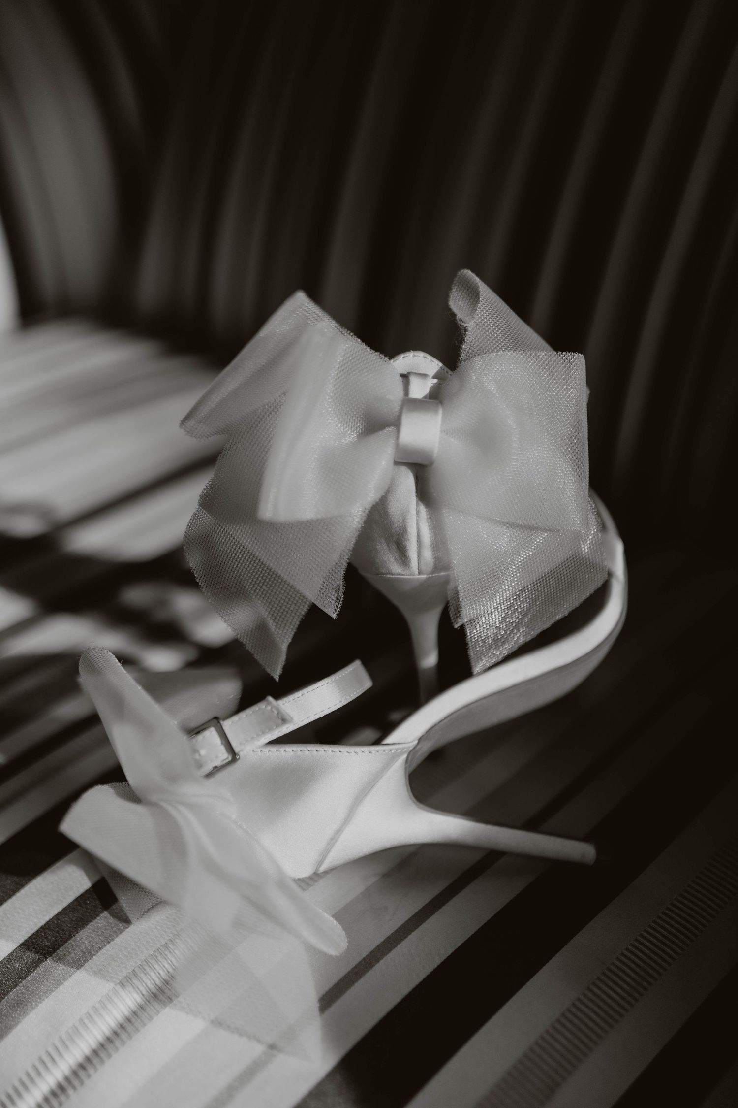 Elegant white bridal shoes with delicate tulle bows and stiletto heels photographed in black and white.