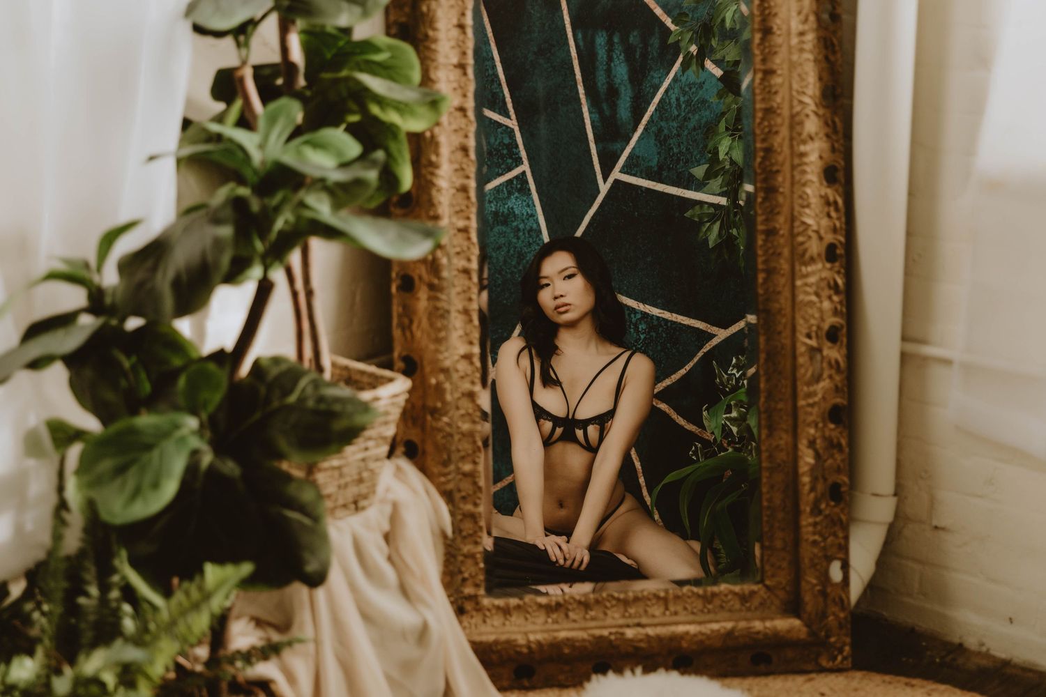 Artistic boudoir photograph displayed in an ornate gold frame with plants in foreground.