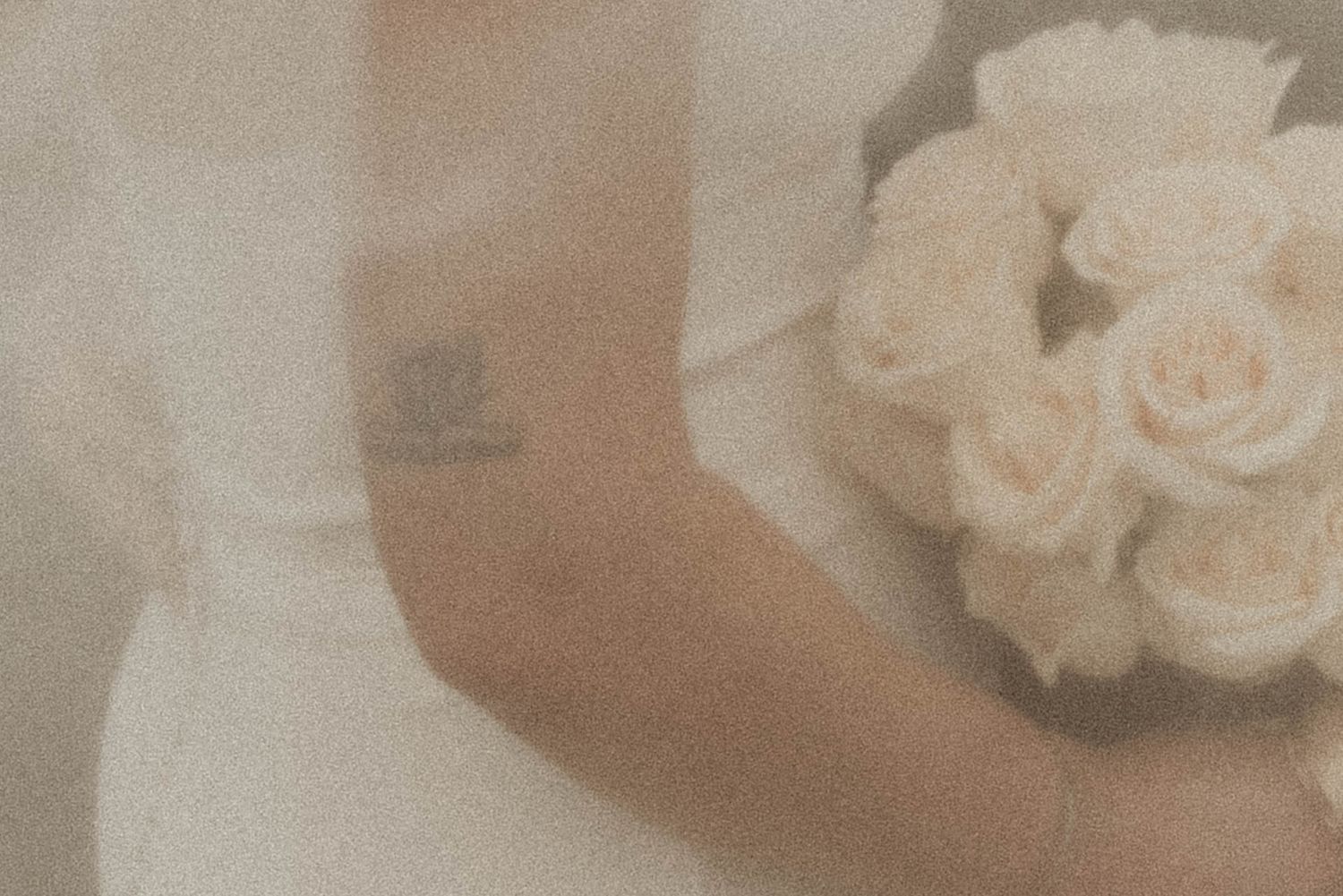 Elegant white roses in a bridal bouquet with soft focus wedding dress details.