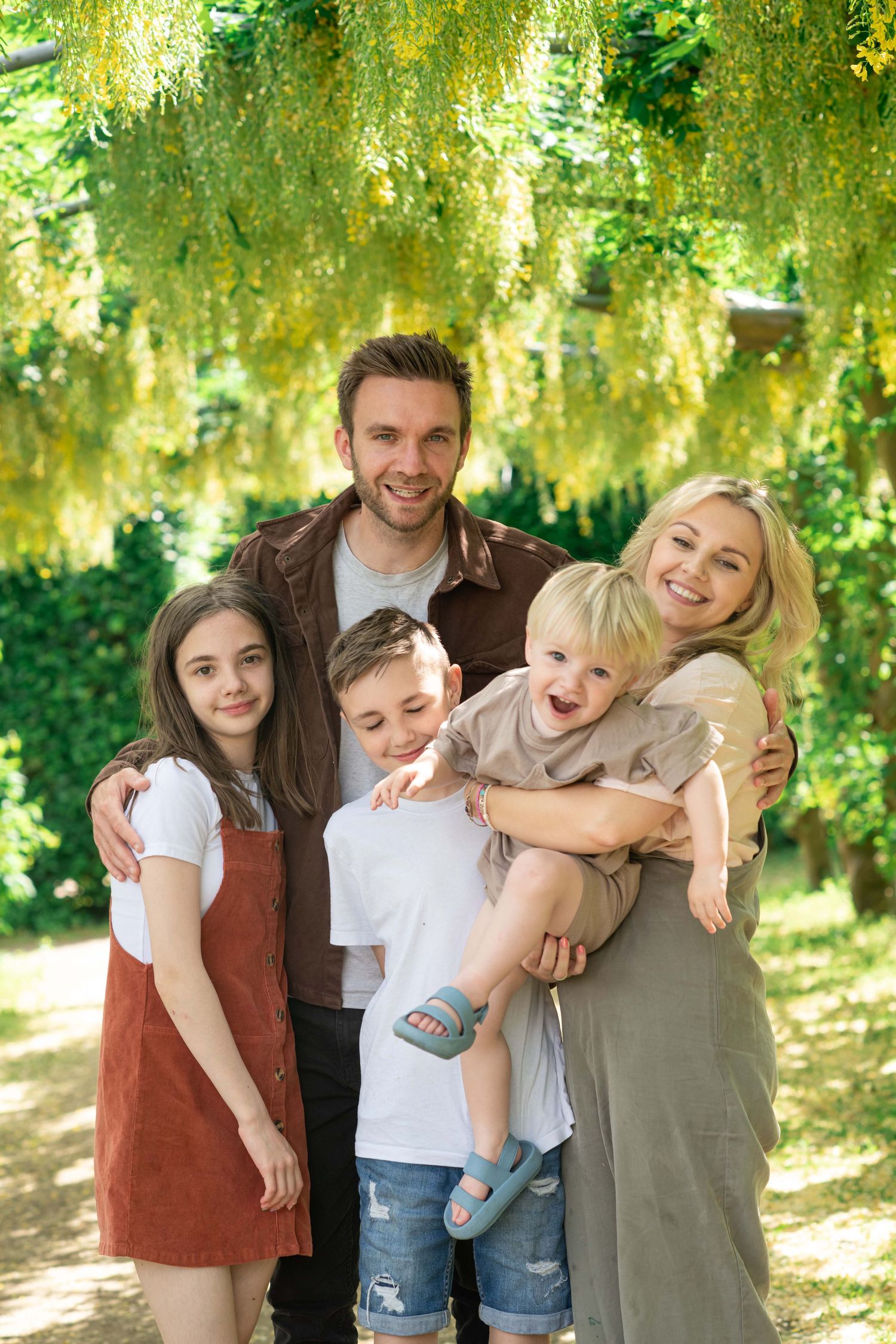 Family enjoying a sunny day together under beautiful yellow flowering trees in a park.