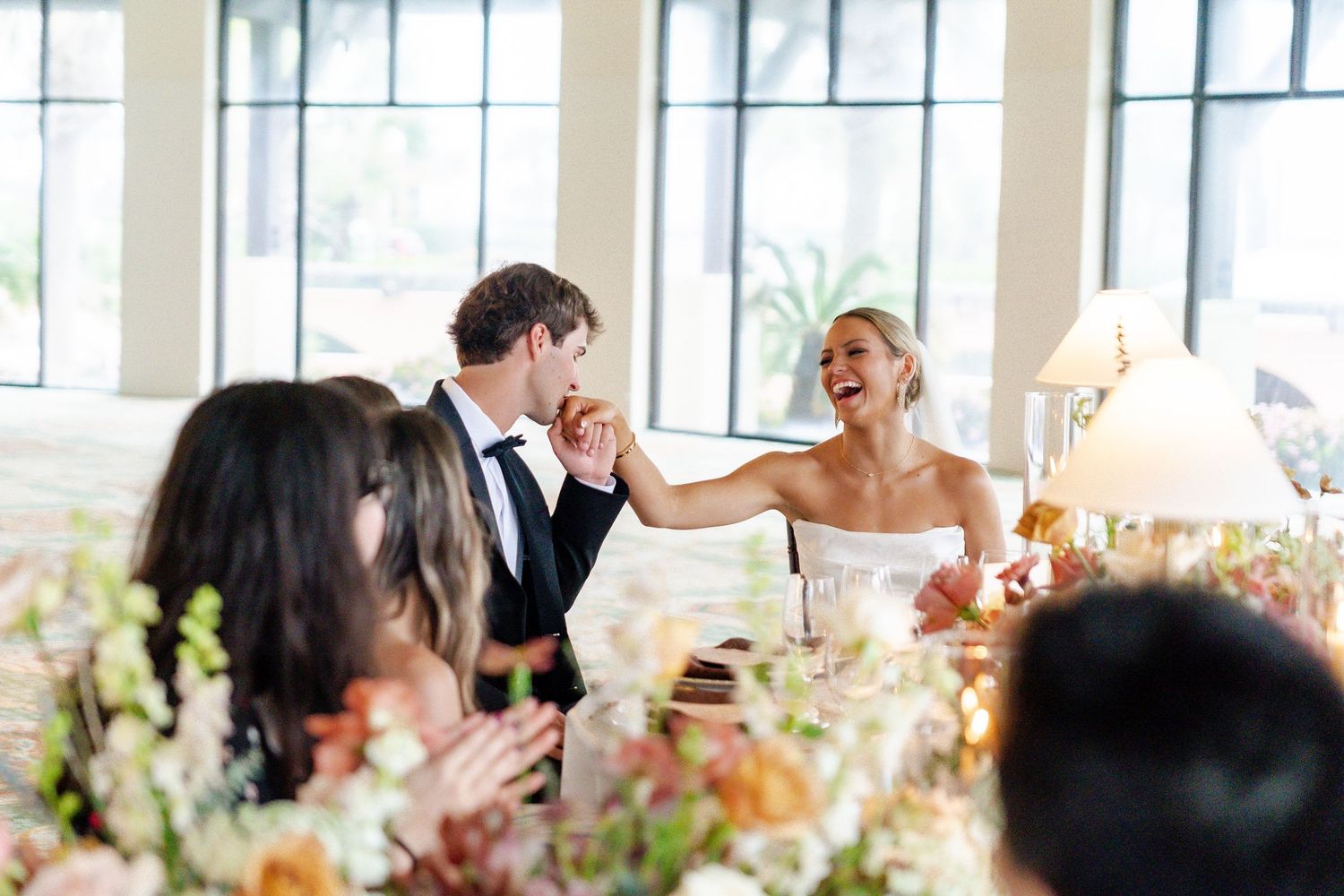 Couple shares a joyful moment with guests at an elegant wedding reception adorned with floral centerpieces.
