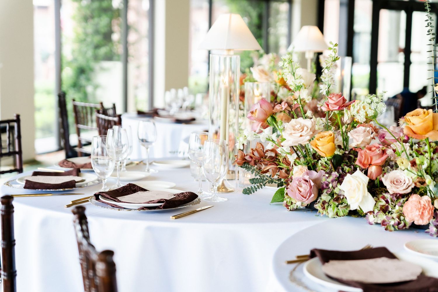 Elegant wedding reception table setting with white linens and lush floral centerpiece featuring pink and peach roses.