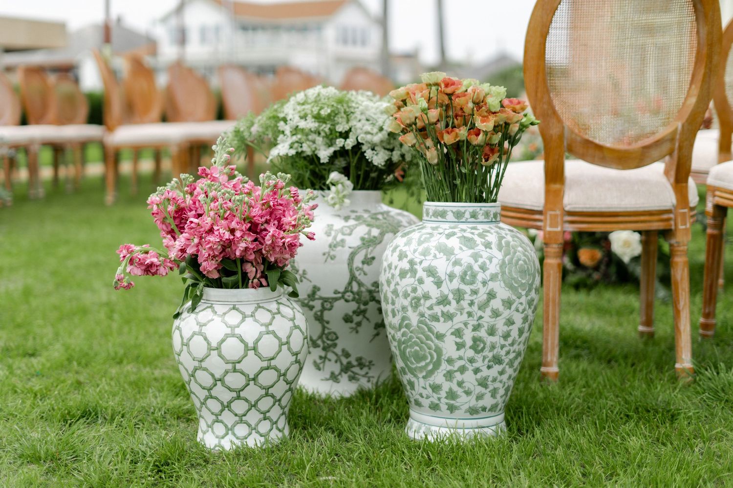 Elegant blue and white chinoiserie vases filled with pink and white flowers arranged on green grass at an outdoor event.