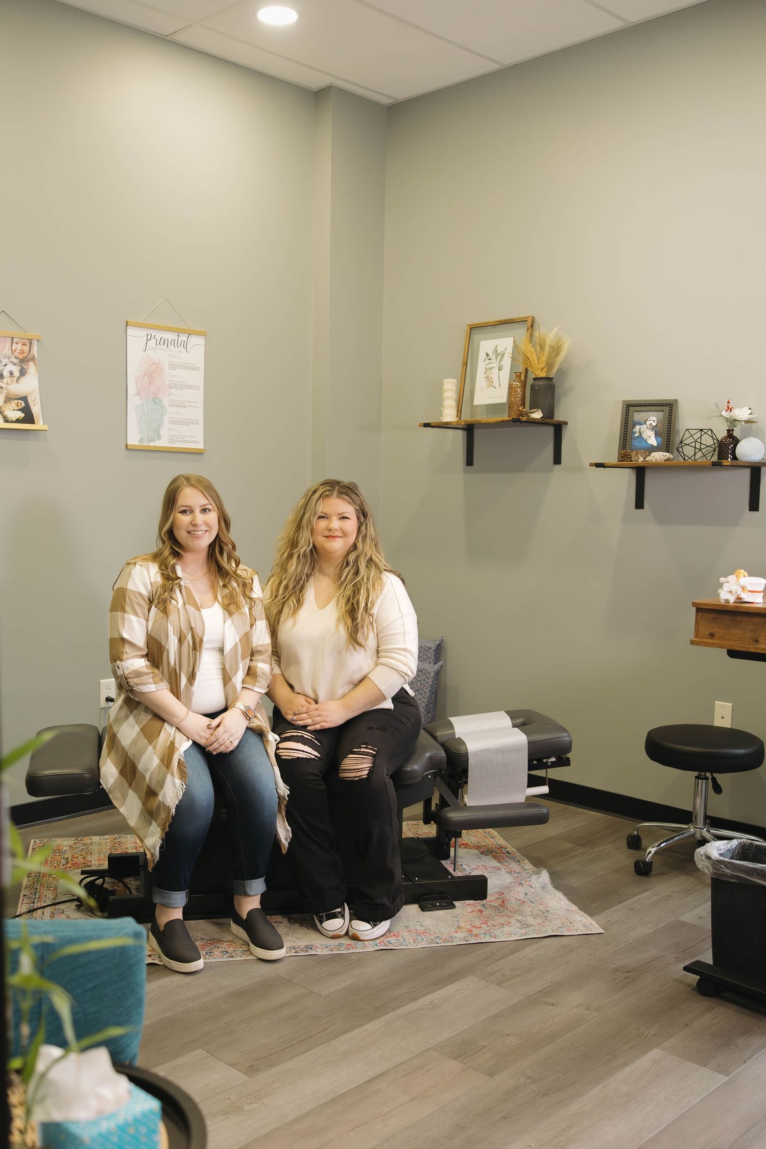 Two people sitting on chairs in a modern medical office or spa room with gray walls and floating shelves. Kansas City wedding photographer.