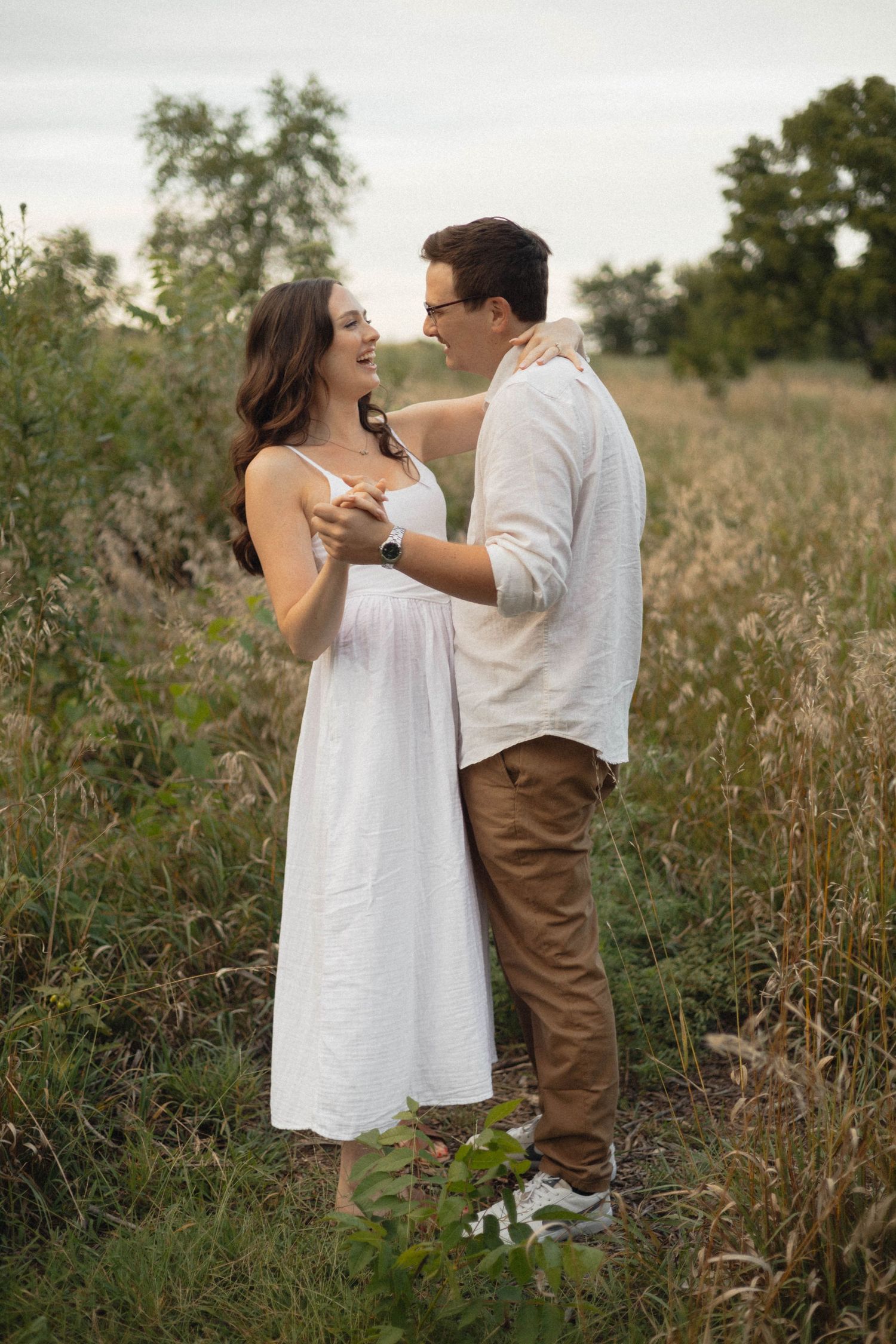 A couple shares a romantic moment while dancing in a sunlit meadow filled with tall grasses and wildflowers. KC area photographer.