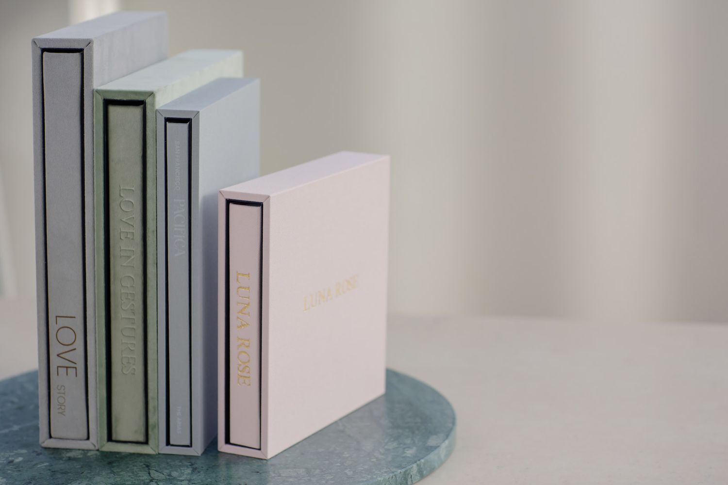 Minimalist aesthetic with four hardcover books standing upright on a blue-tinted surface against a neutral background.