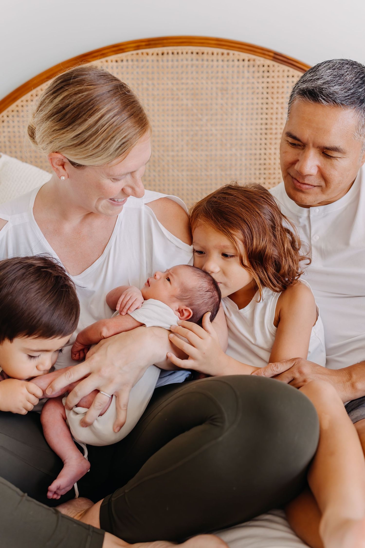 Intimate family moment showing parents with their children gathered on chair to admire newborn baby.