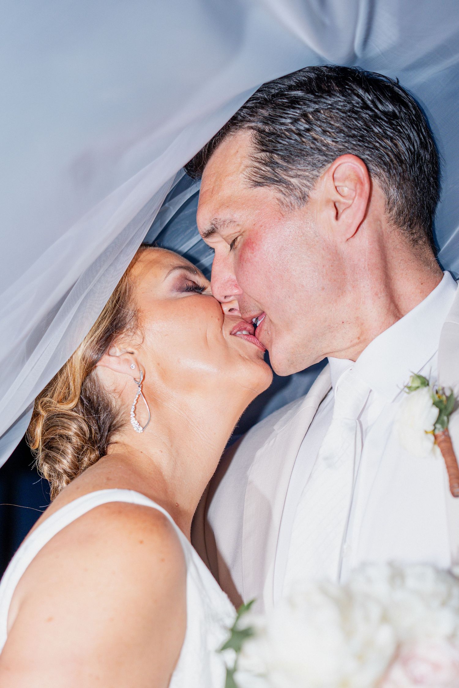 A bride and groom share a tender kiss during their wedding ceremony while wearing traditional white attire.