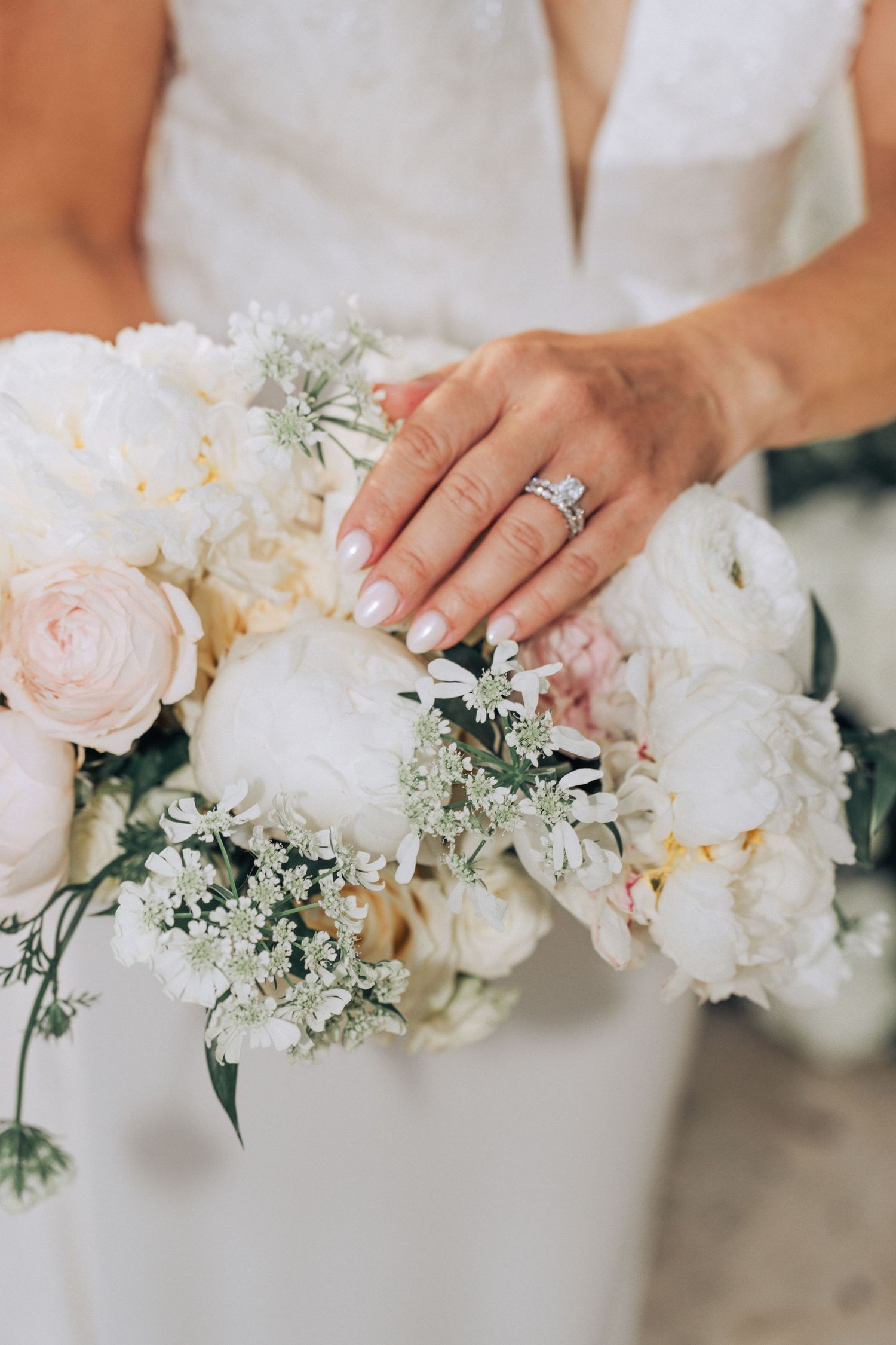 Close-up of bridal bouquet with white and blush peonies, roses and delicate greenery with engagement ring on display.
