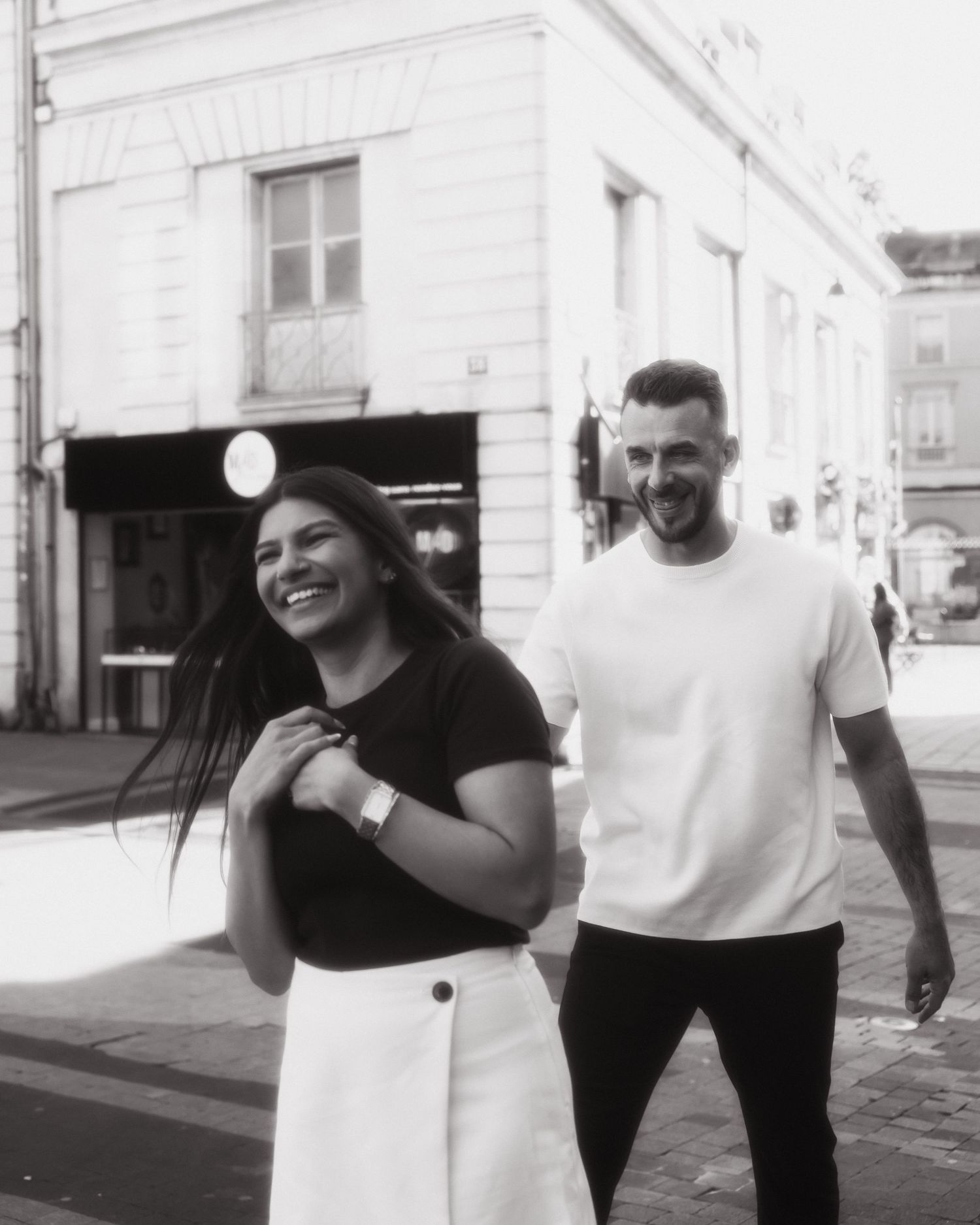 Two people sharing a candid moment on a city street, captured in black and white photography.