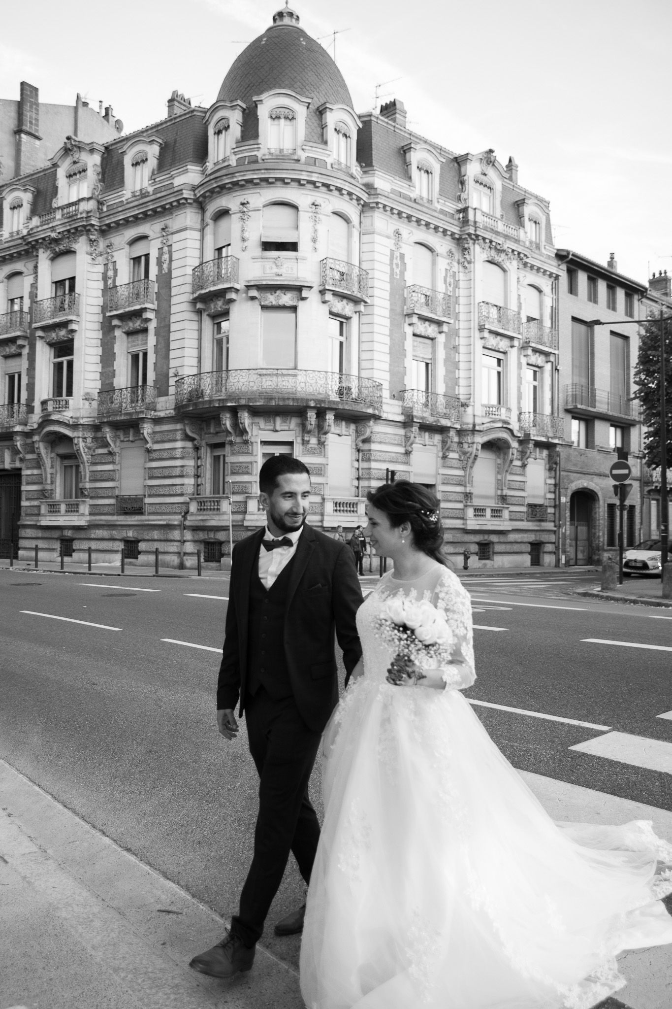 A black and white wedding photo in front of an ornate European building with decorative architecture.