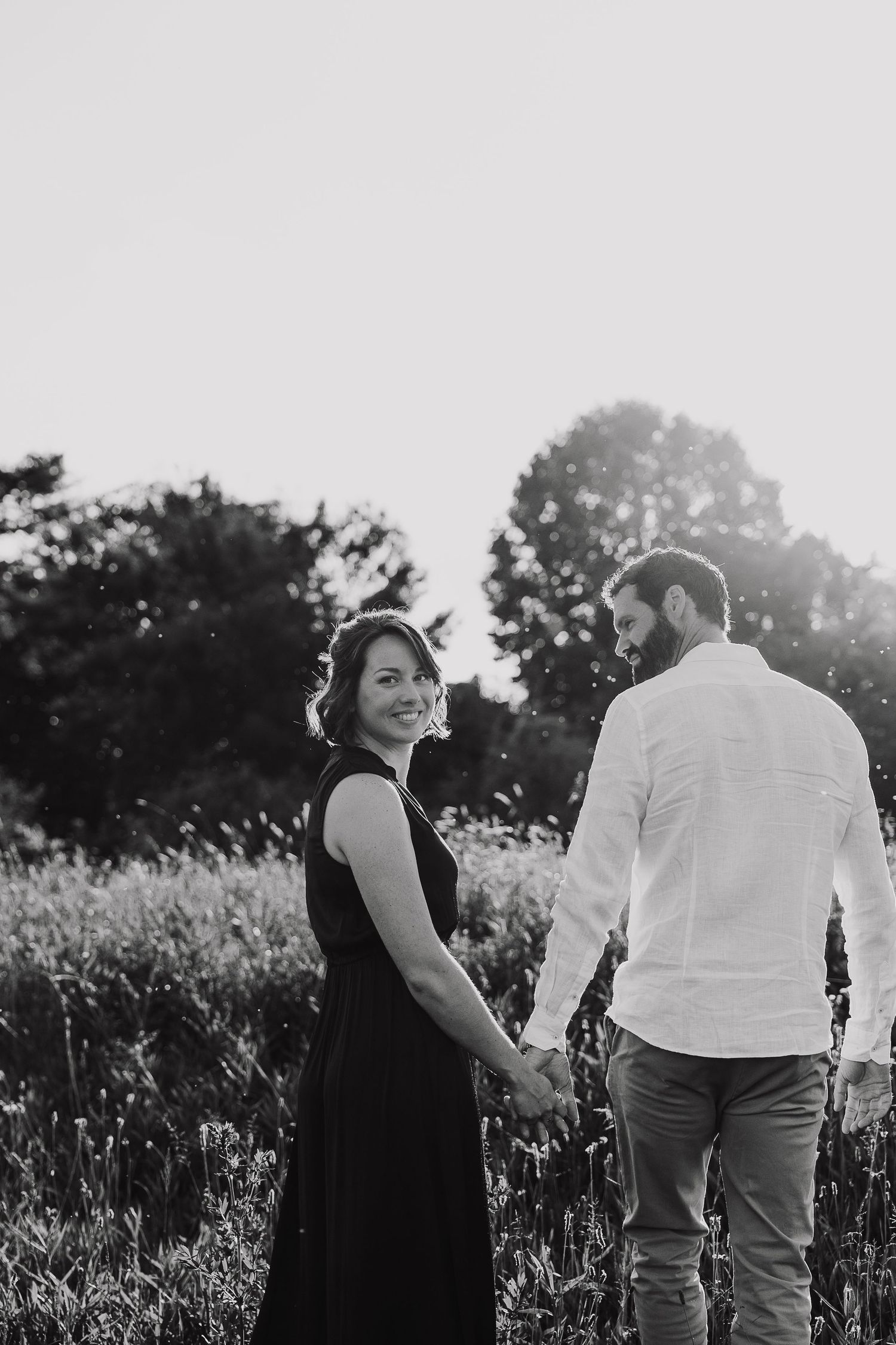A couple stands together in a field of wildflowers during a golden sunset photoshoot.