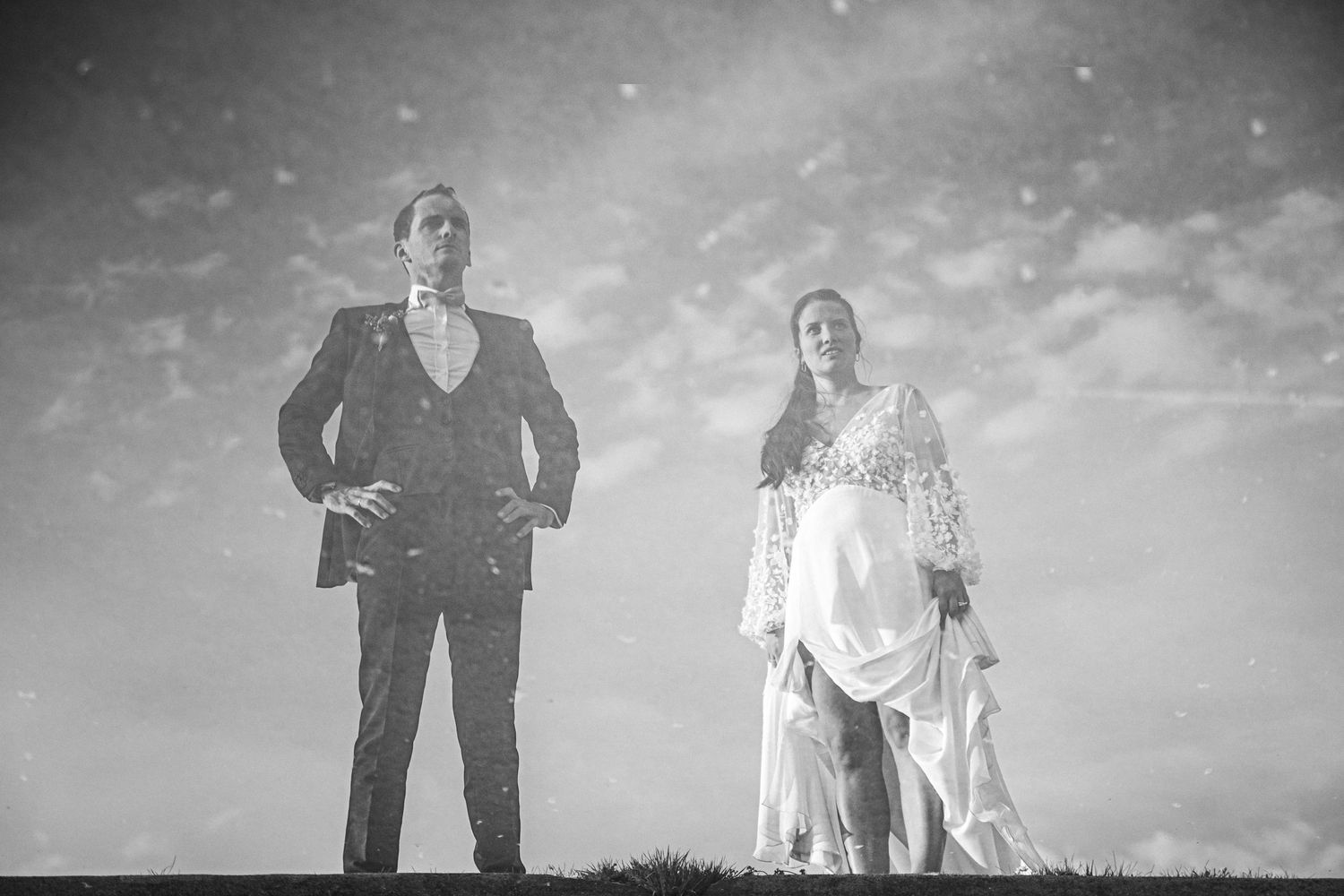 Artistic black and white portrait of wedding couple standing on hilltop under cloudy sky.