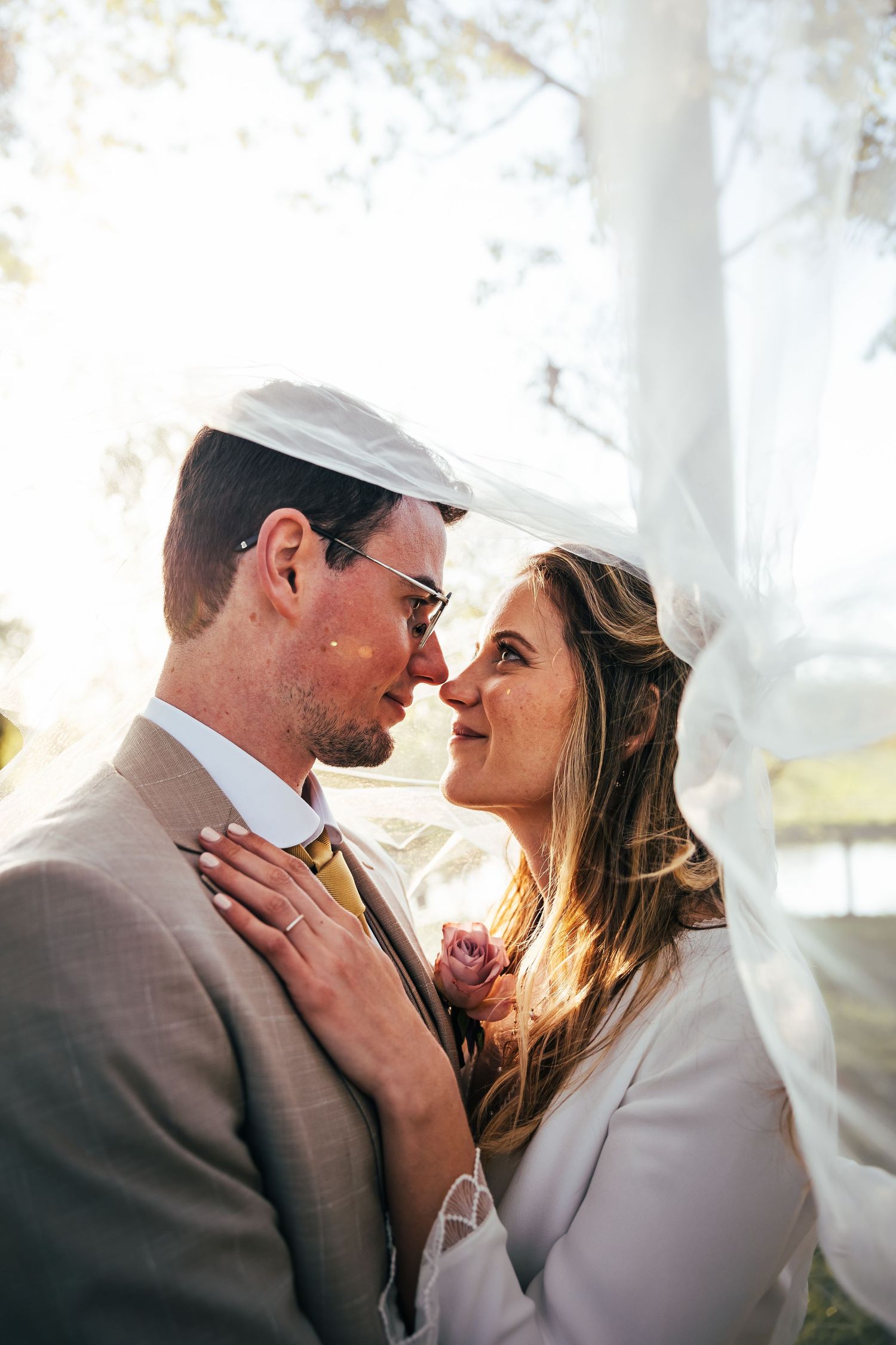 Romantic wedding couple shares an intimate moment bathed in soft sunlight through white curtains.