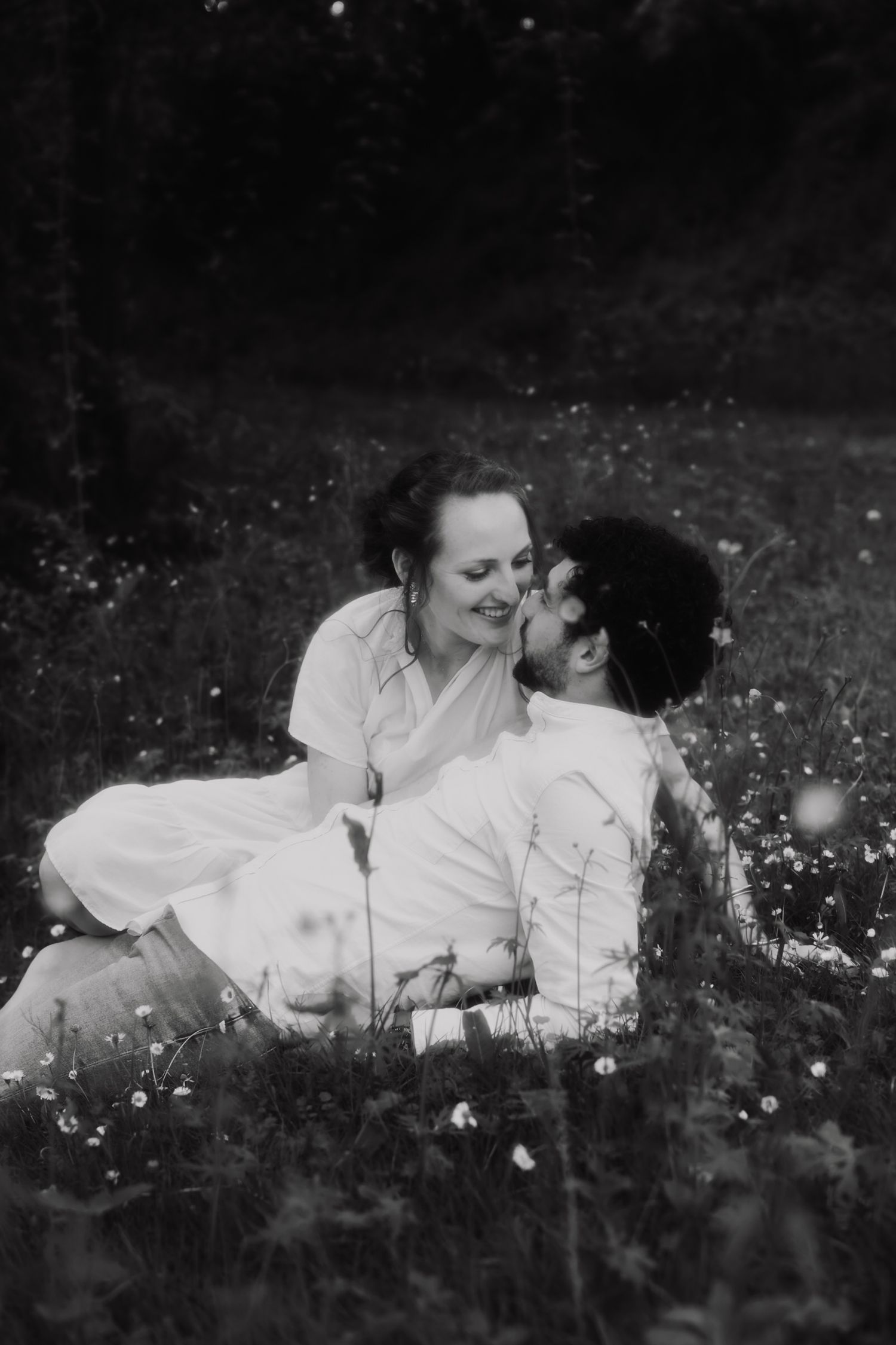 A sequence showing someone in a white dress lying down in a meadow of wildflowers in black and white.