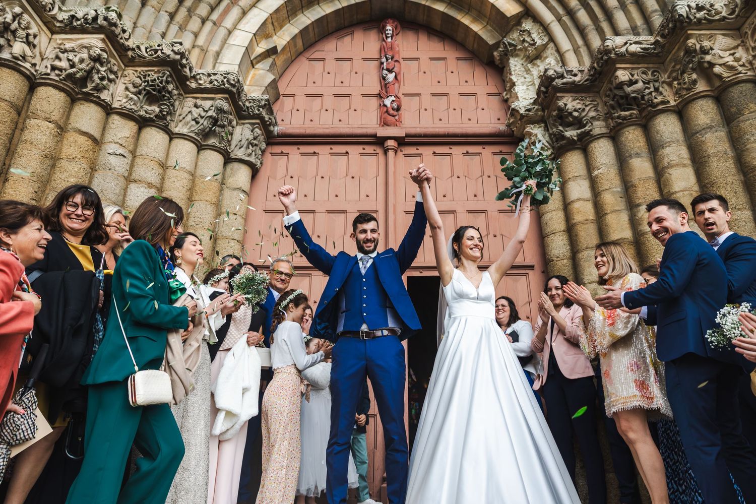 Newlyweds celebrate outside historic church entrance as guests cheer with confetti.