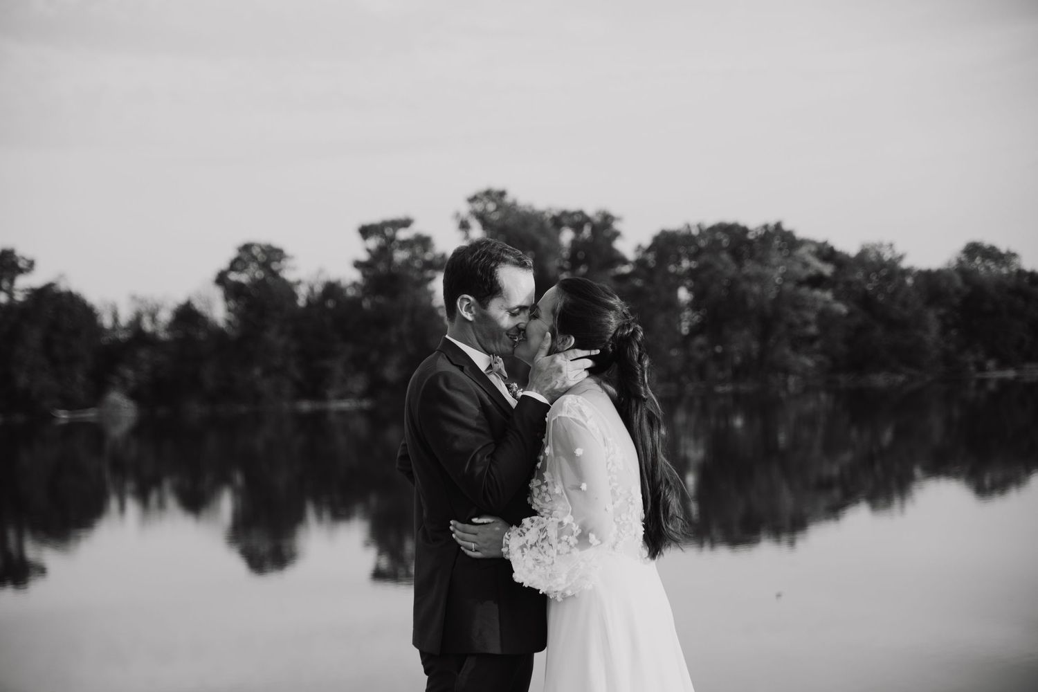 Intimate black and white portrait of newlyweds by serene lakeside reflection.