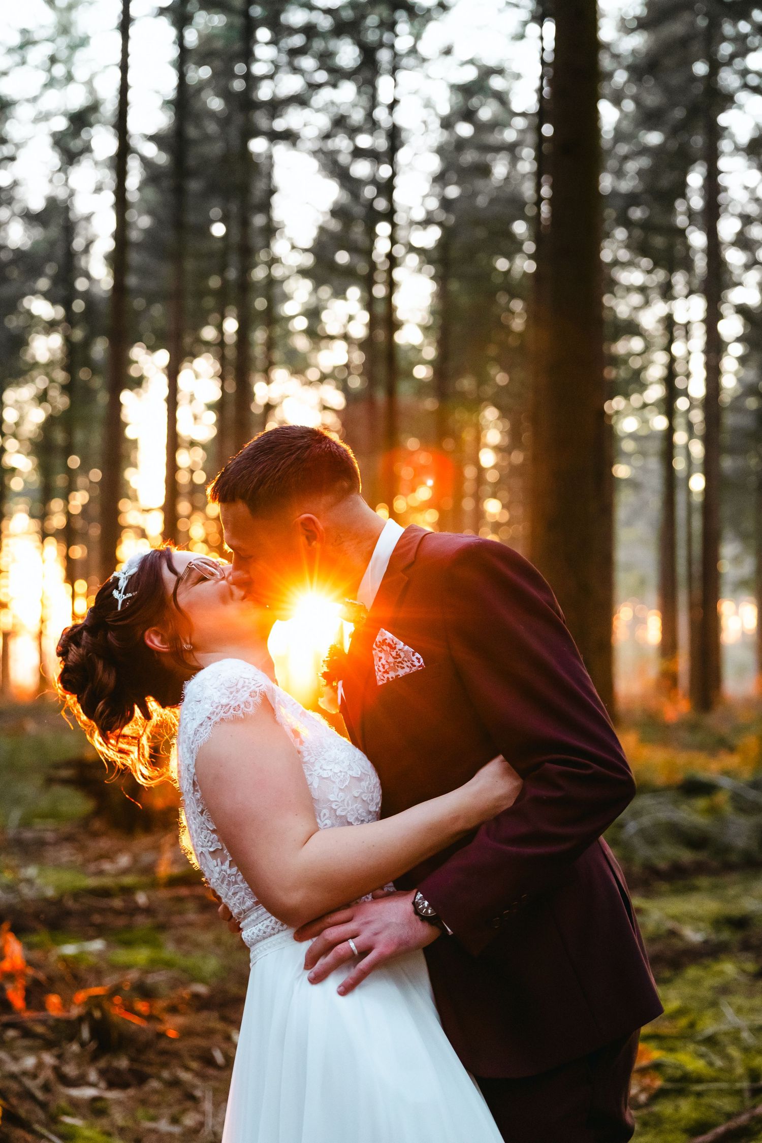 Newlyweds kiss in a sunlit forest at golden hour creating a magical wedding moment.