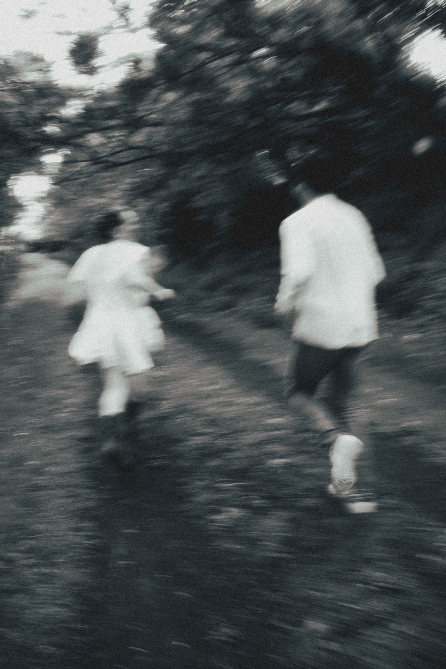 Blurred motion black and white photograph of two people in white clothing running on a dark trail.