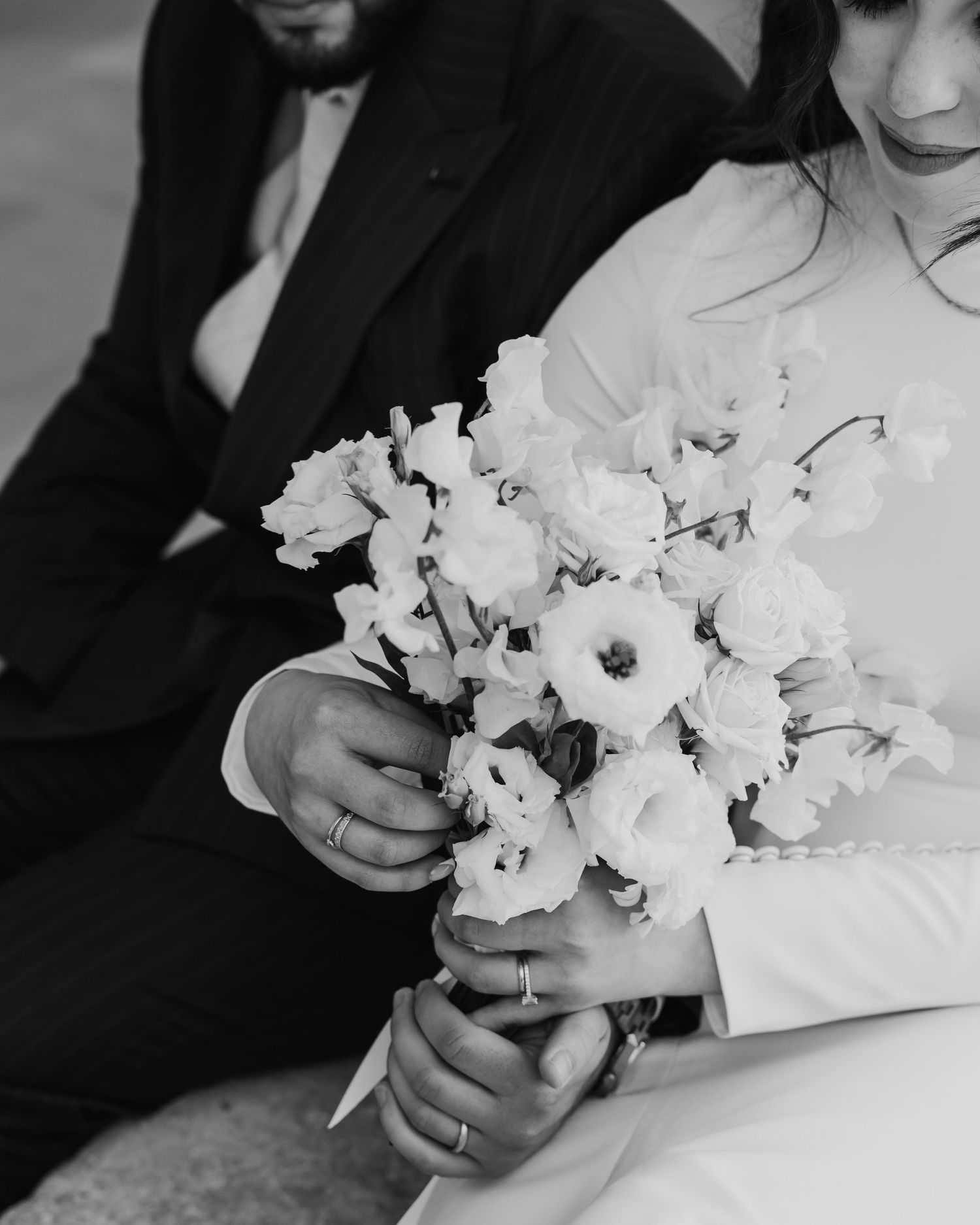 Black and white wedding photo showing hands holding an elegant white floral bouquet with rose and anemone flowers.