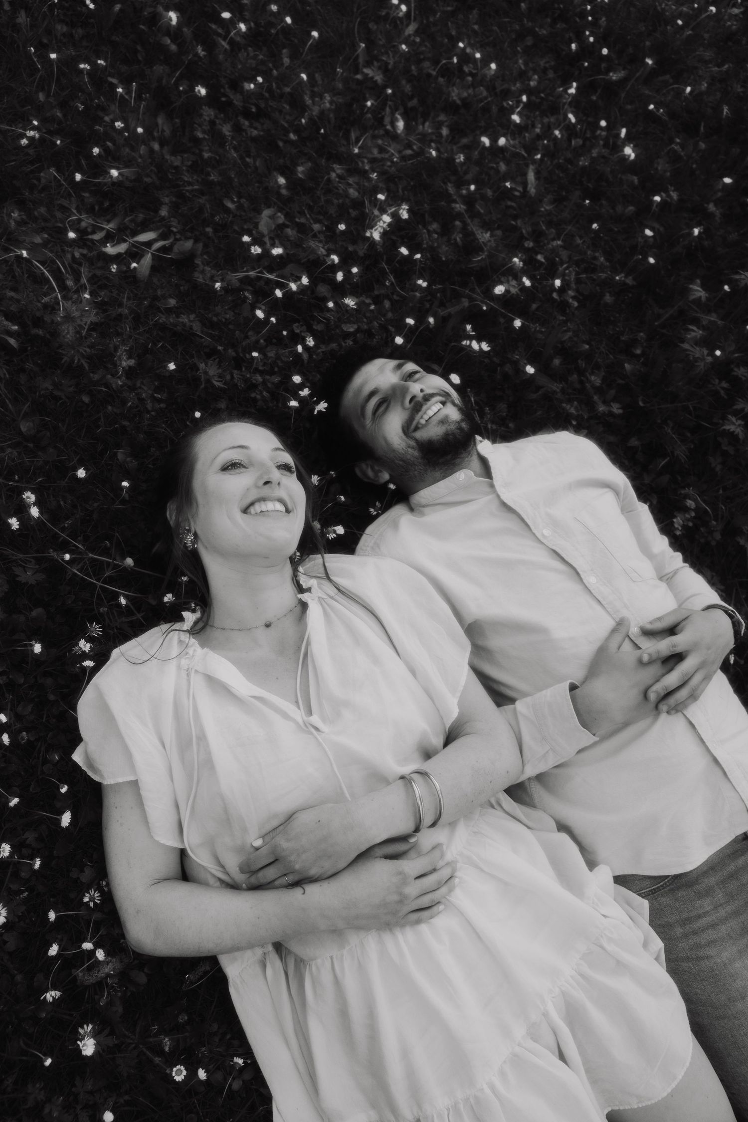 A couple in white outfits laughing together outdoors in a candid black and white photo.