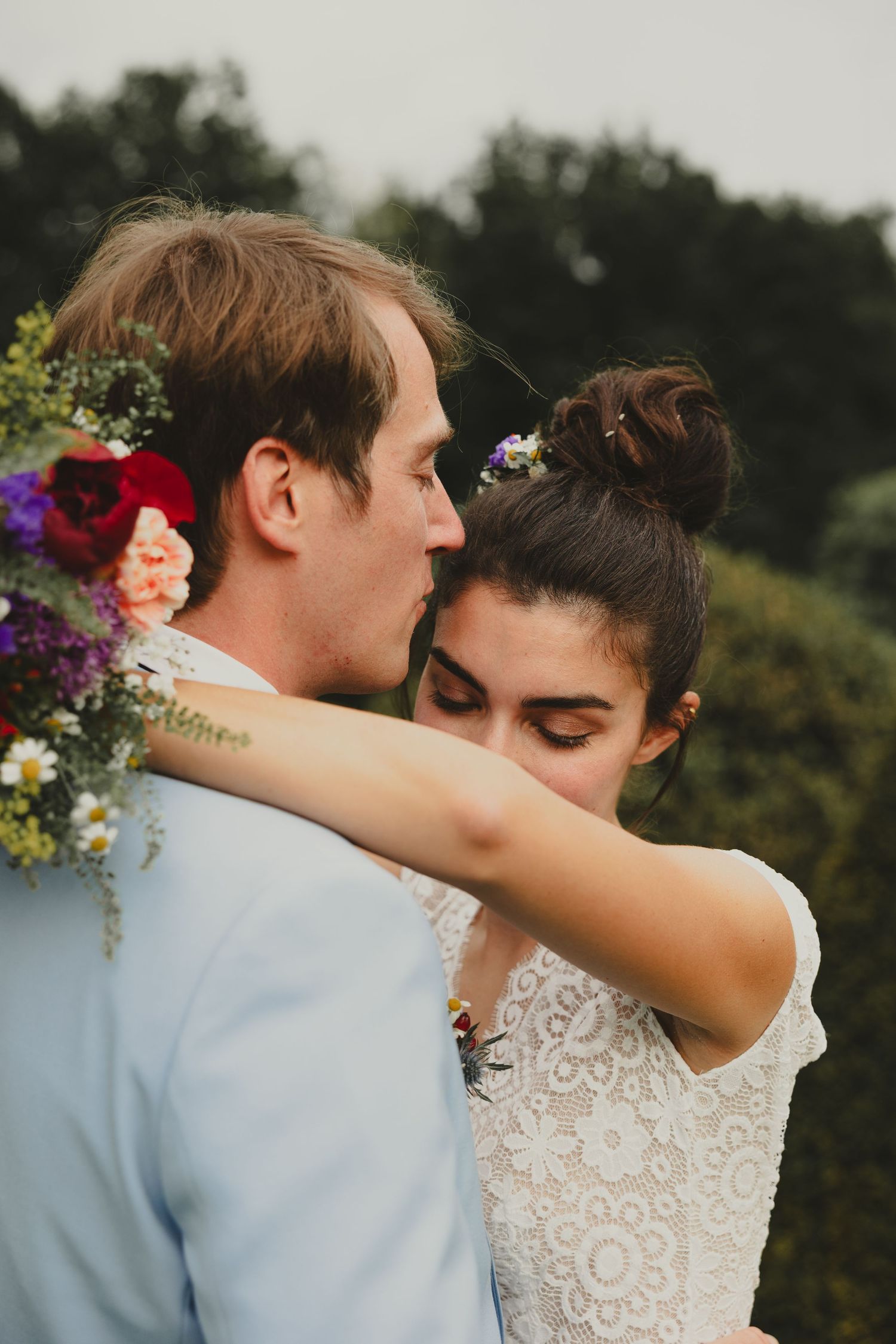 Couple shares intimate wedding day embrace surrounded by vibrant wildflowers and greenery.
