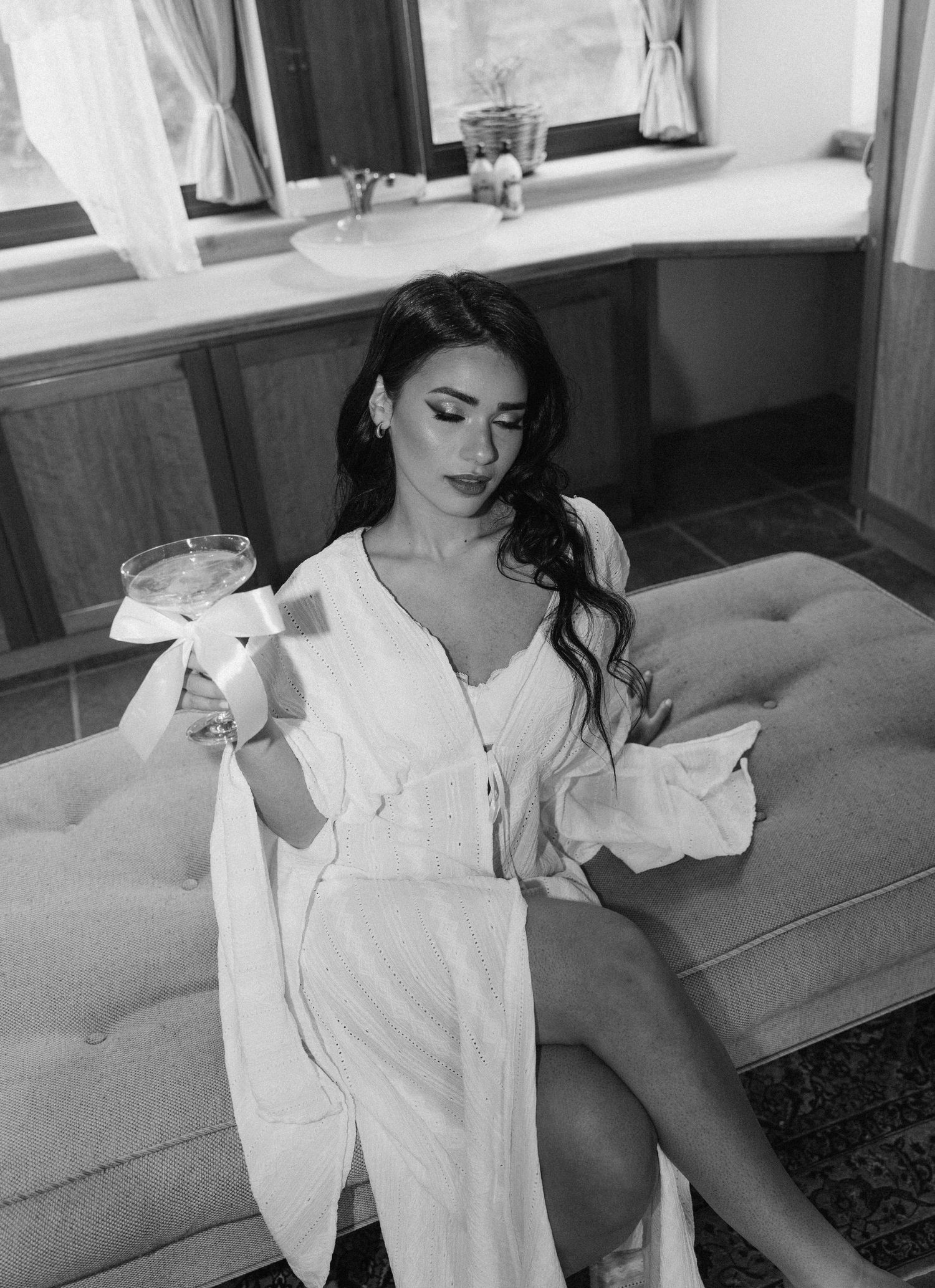 Black and white photo of a woman in a white robe holding a cocktail glass while gettiong ready for her wedding at La Roche, Franschhoek.