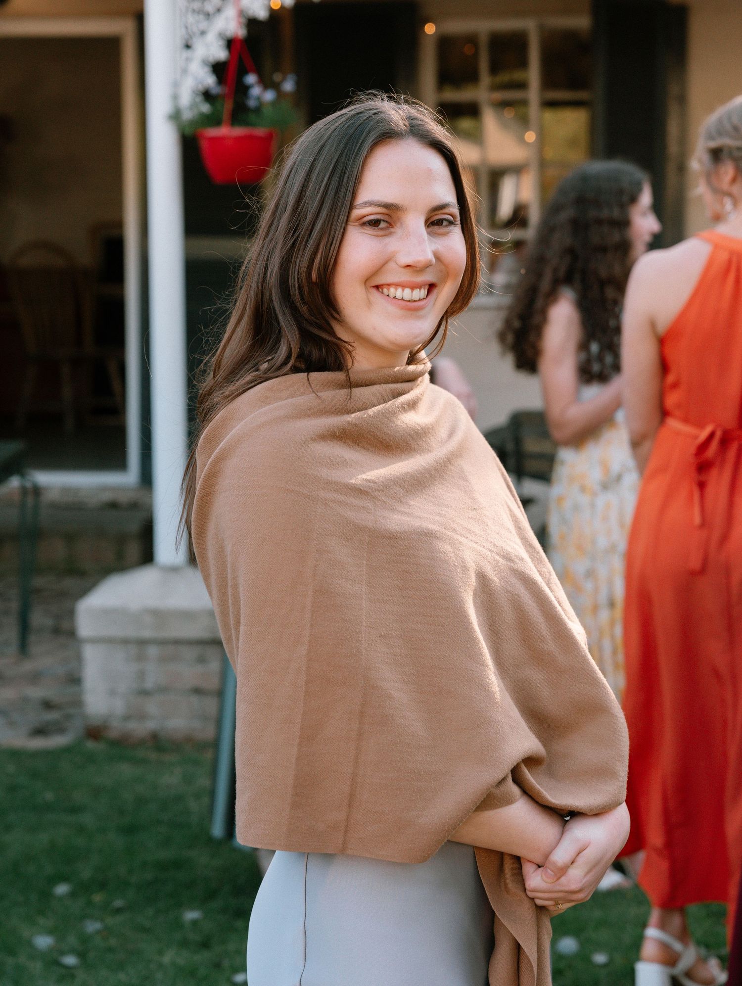 Woman in beige wrap smiles at outdoor event.