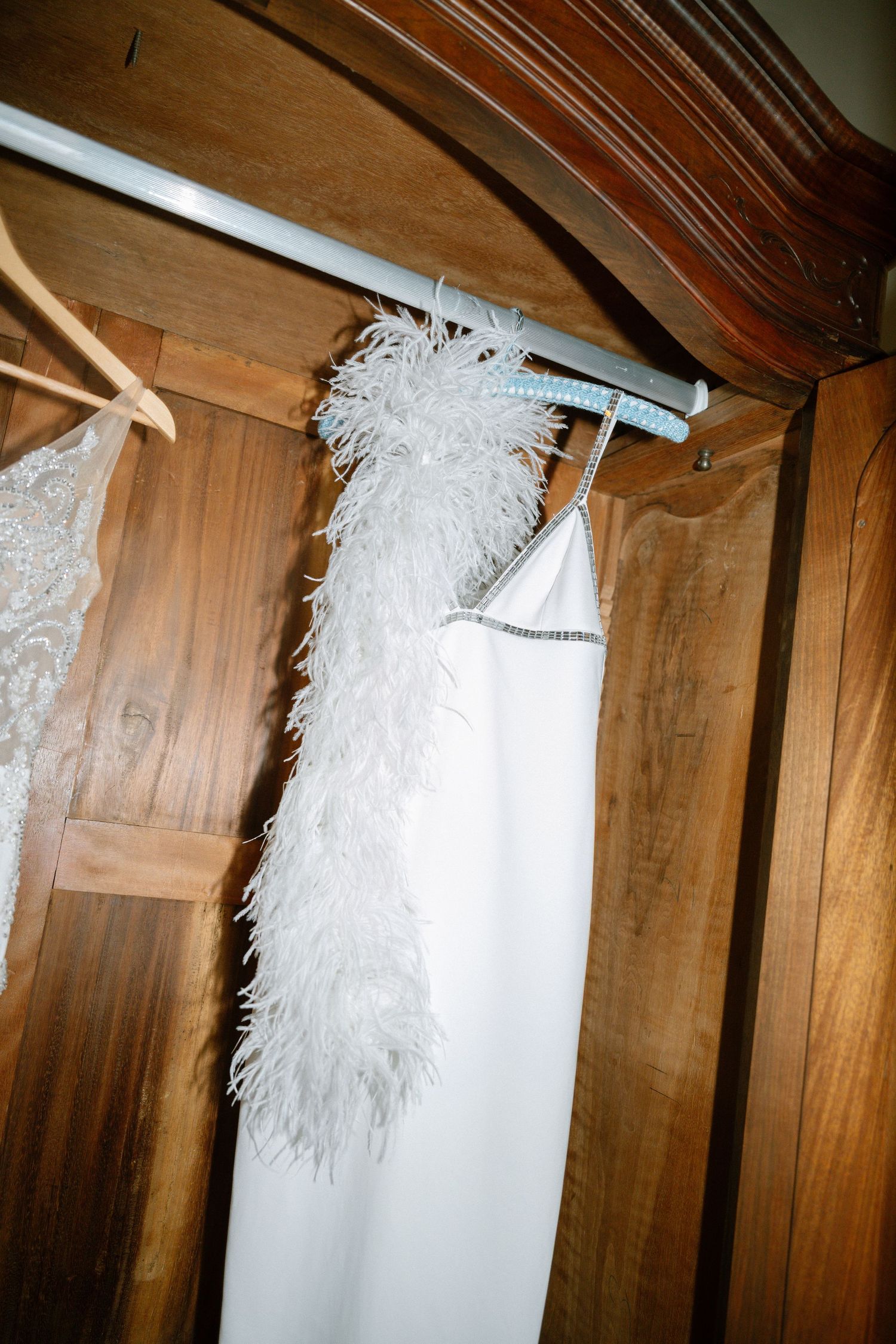 A white feathered wedding dress hanging on a wooden wardrobe.