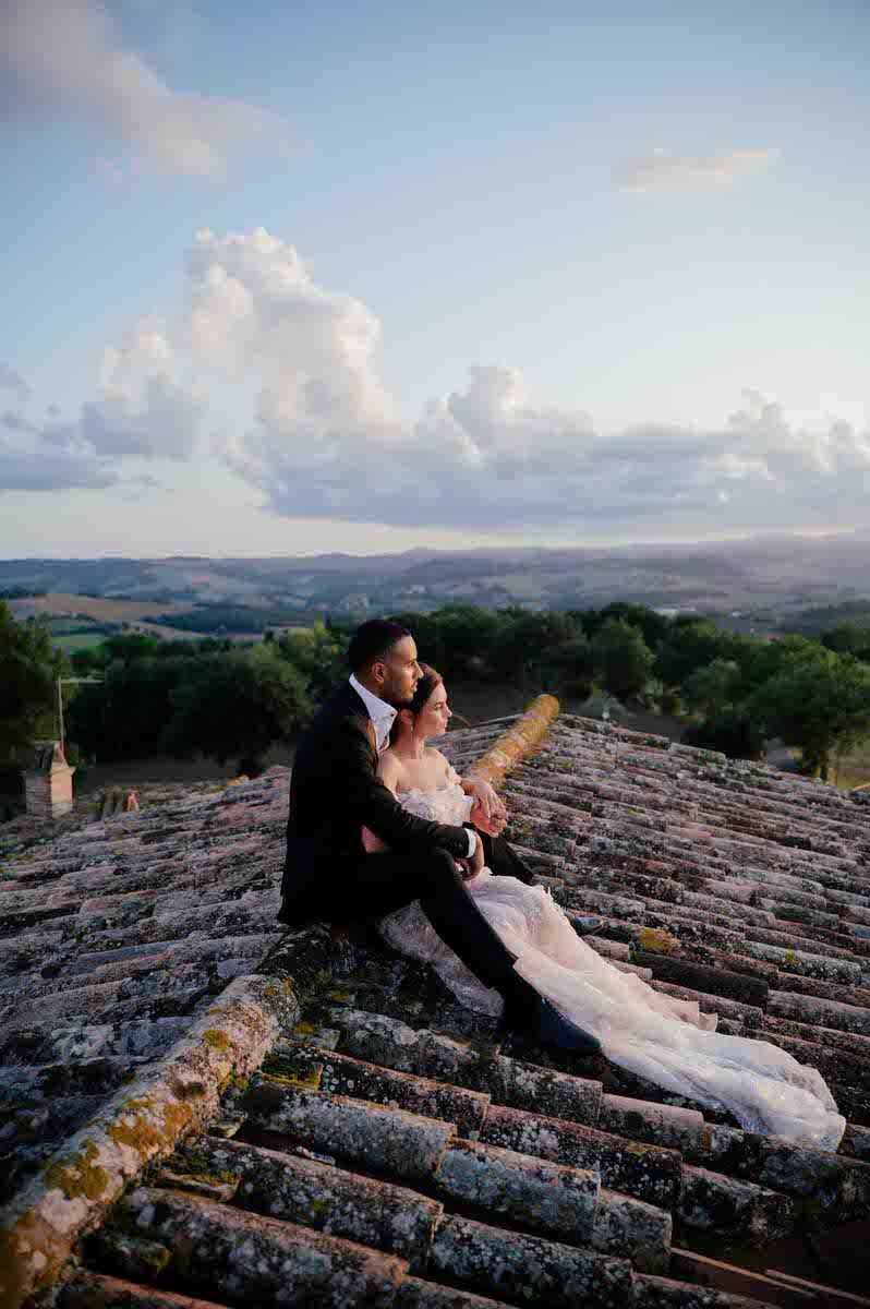 Newlyweds share intimate moment on ancient tiled rooftop overlooking Tuscan landscape.