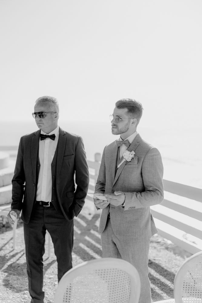 Two men in formal attire stand together at an outdoor venue in black and white.